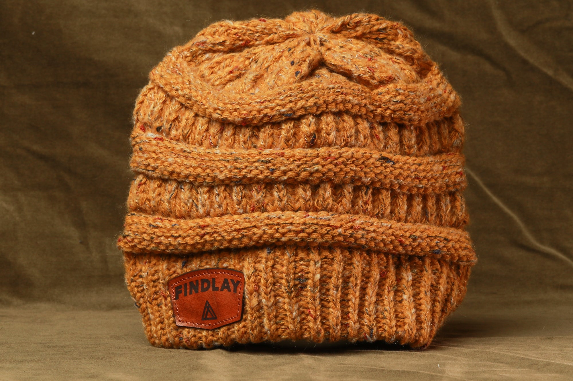 A cozy, knitted beanie with a textured pattern and a small orange patch on the front, sitting on a brown surface.