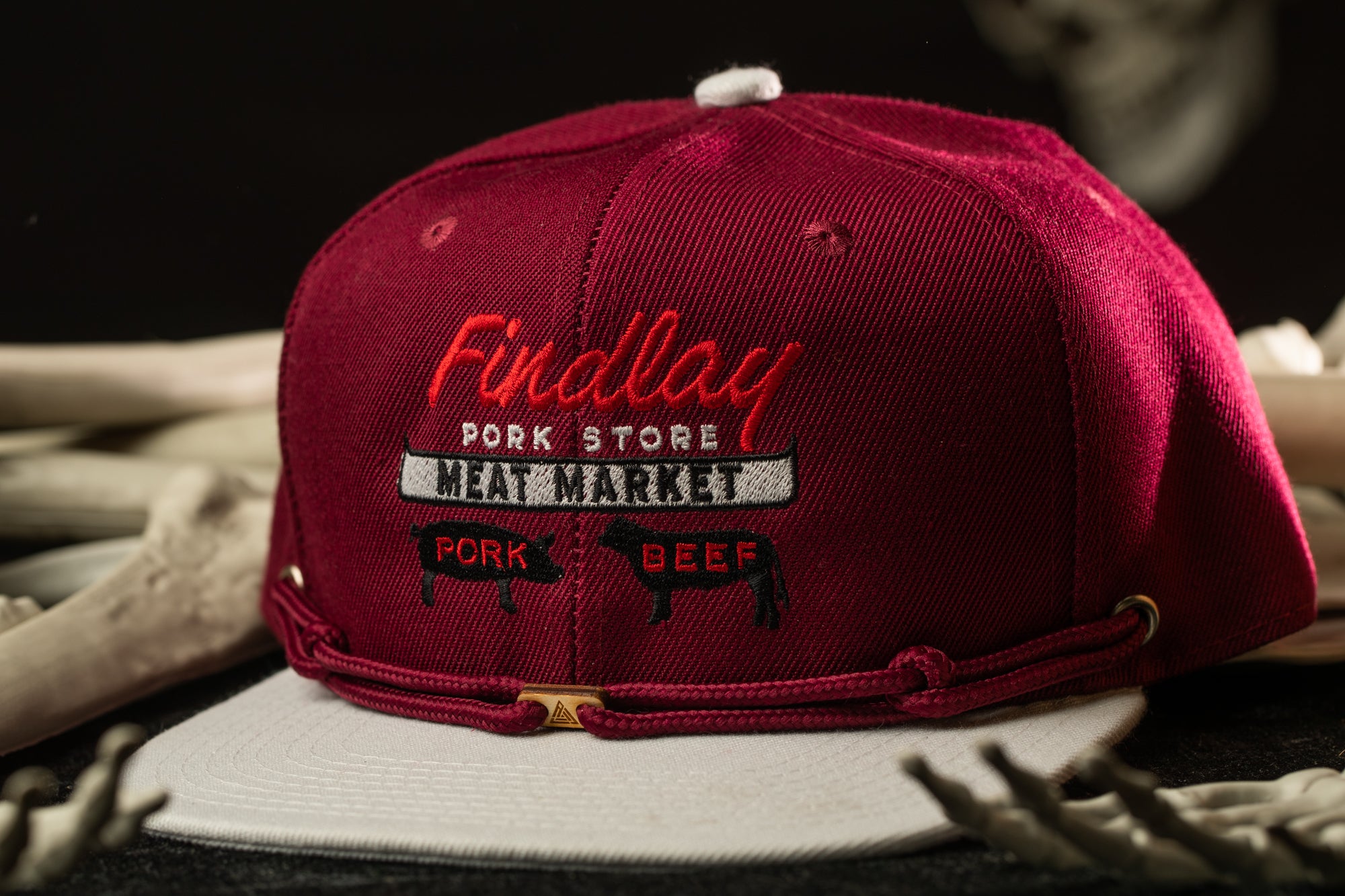 A maroon baseball cap with the text "Findlay Pork Store Meat Market" printed on it, along with images of pork and beef.