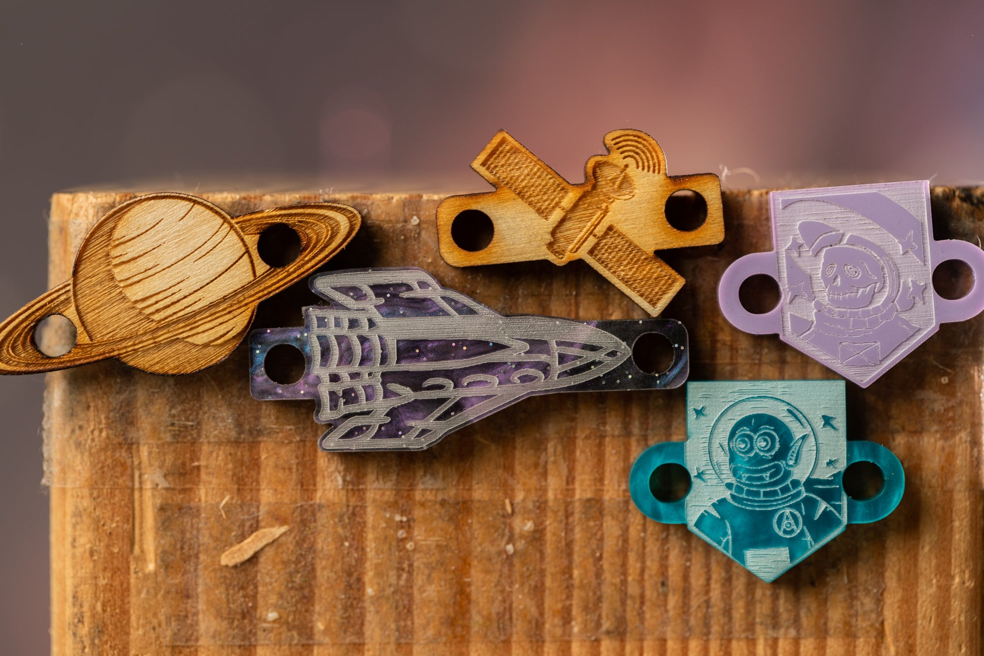 a collection of five wooden or metal objects, including a planet, a rocket ship, a robot, a shield, and a shield with a face, all displayed on a wooden surface.