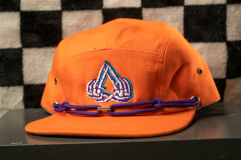 An orange baseball cap with a purple band and a white and blue logo on the front, placed on a black surface against a checkered background.