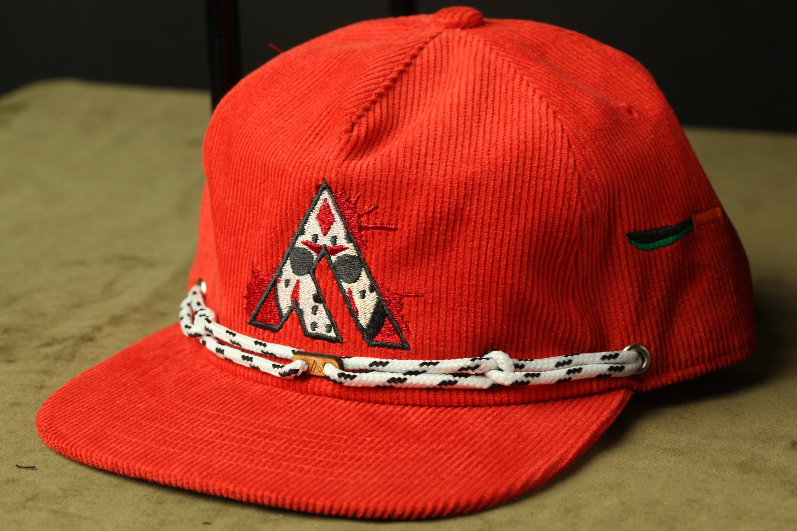 A red baseball cap with a white and black braided band and a logo on the front.