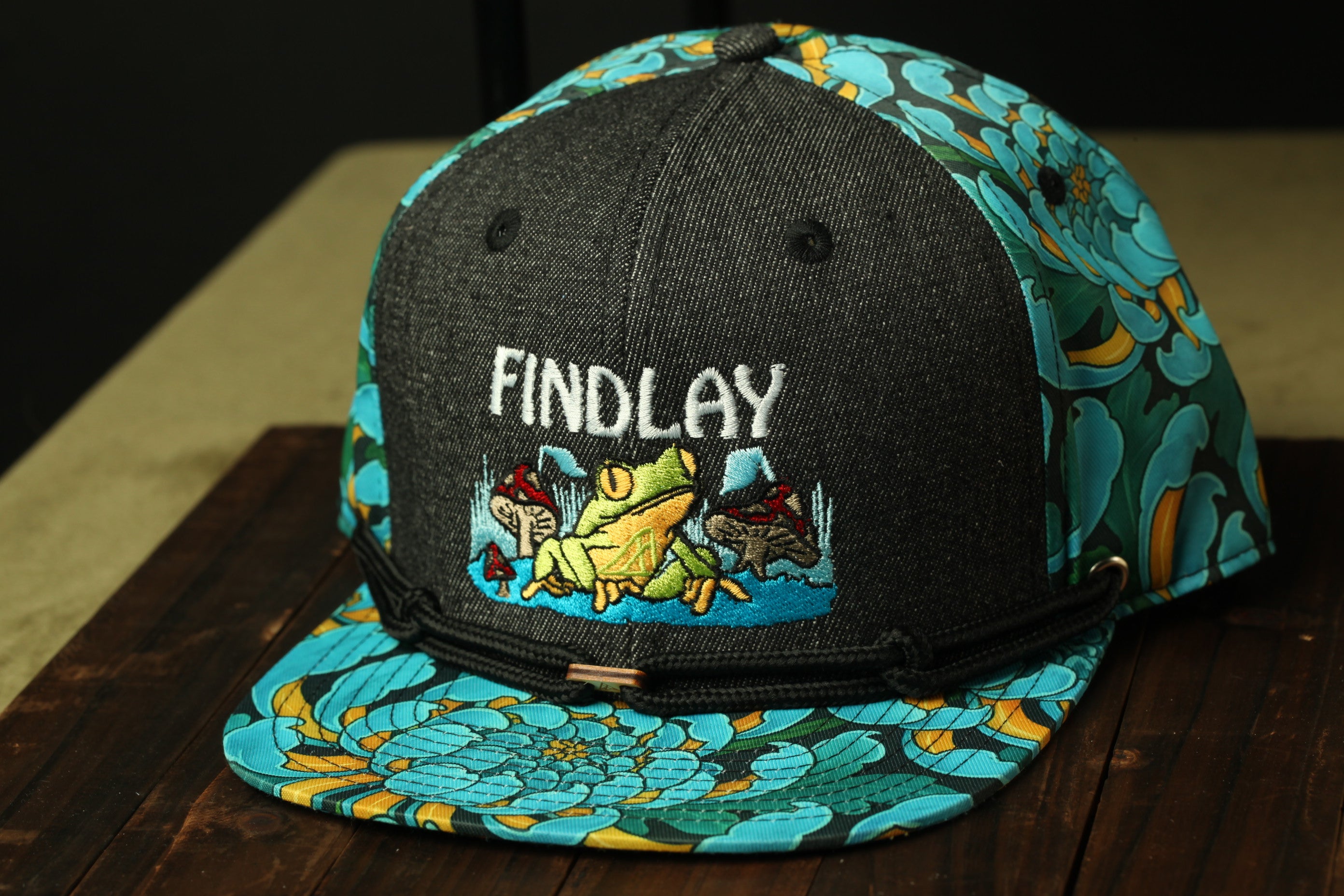 A black baseball cap with a colorful floral pattern and the word "FINDLAY" printed on it.
