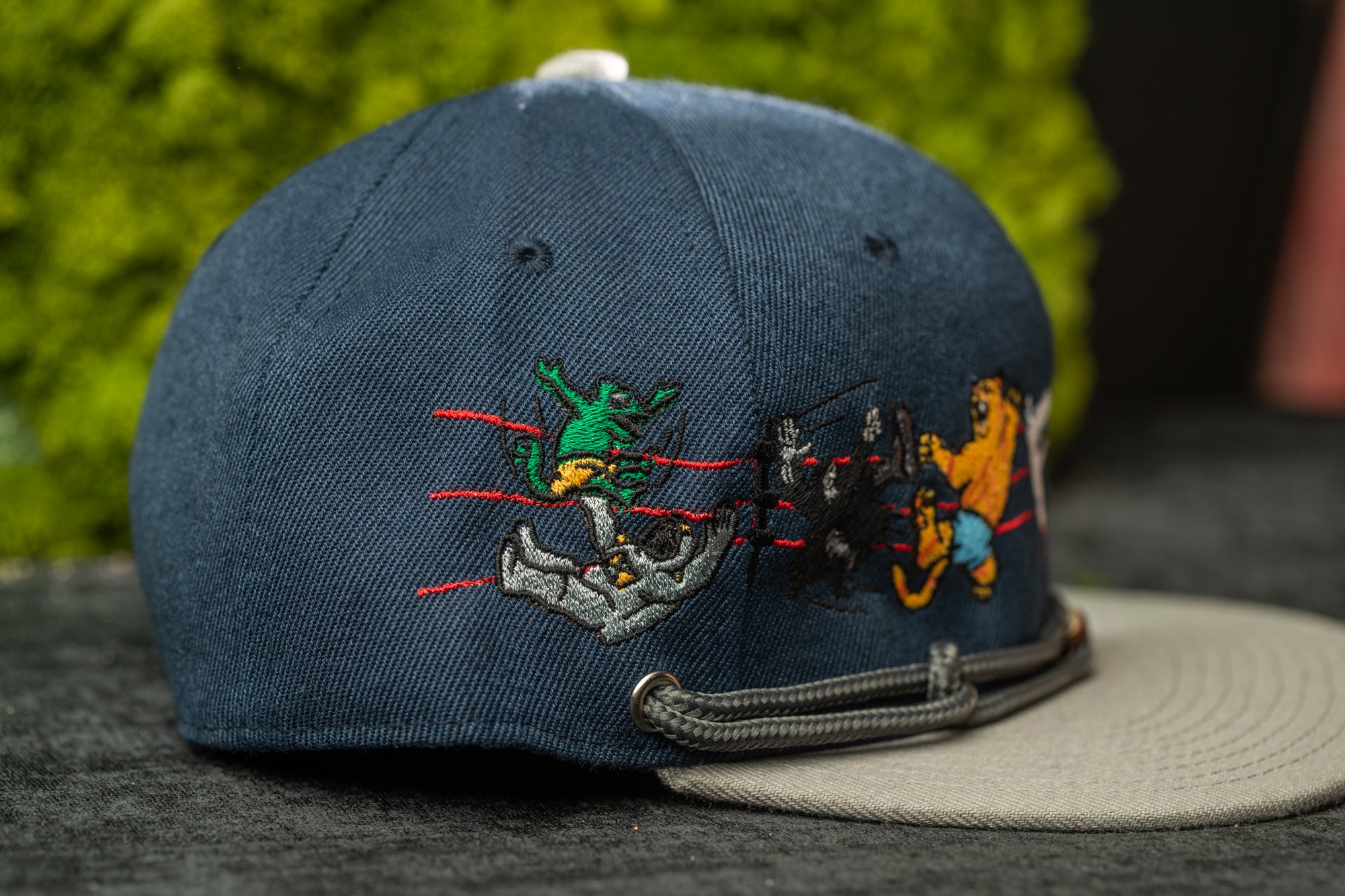 A navy blue baseball cap with colorful cartoon characters and designs on it, including a frog, a cat, and a dog.