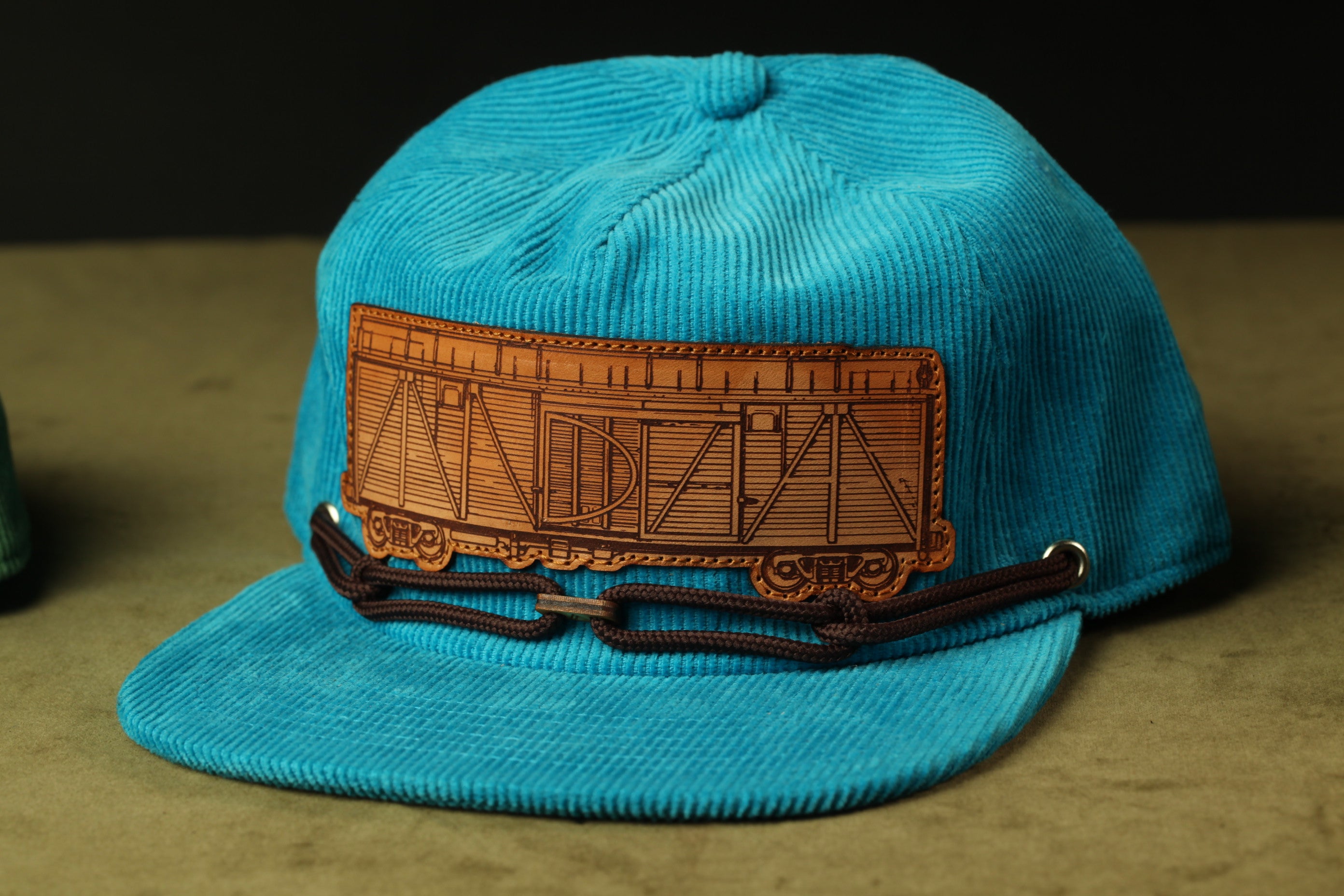 A blue baseball cap with a brown leather patch on the front, featuring an image of a train car.