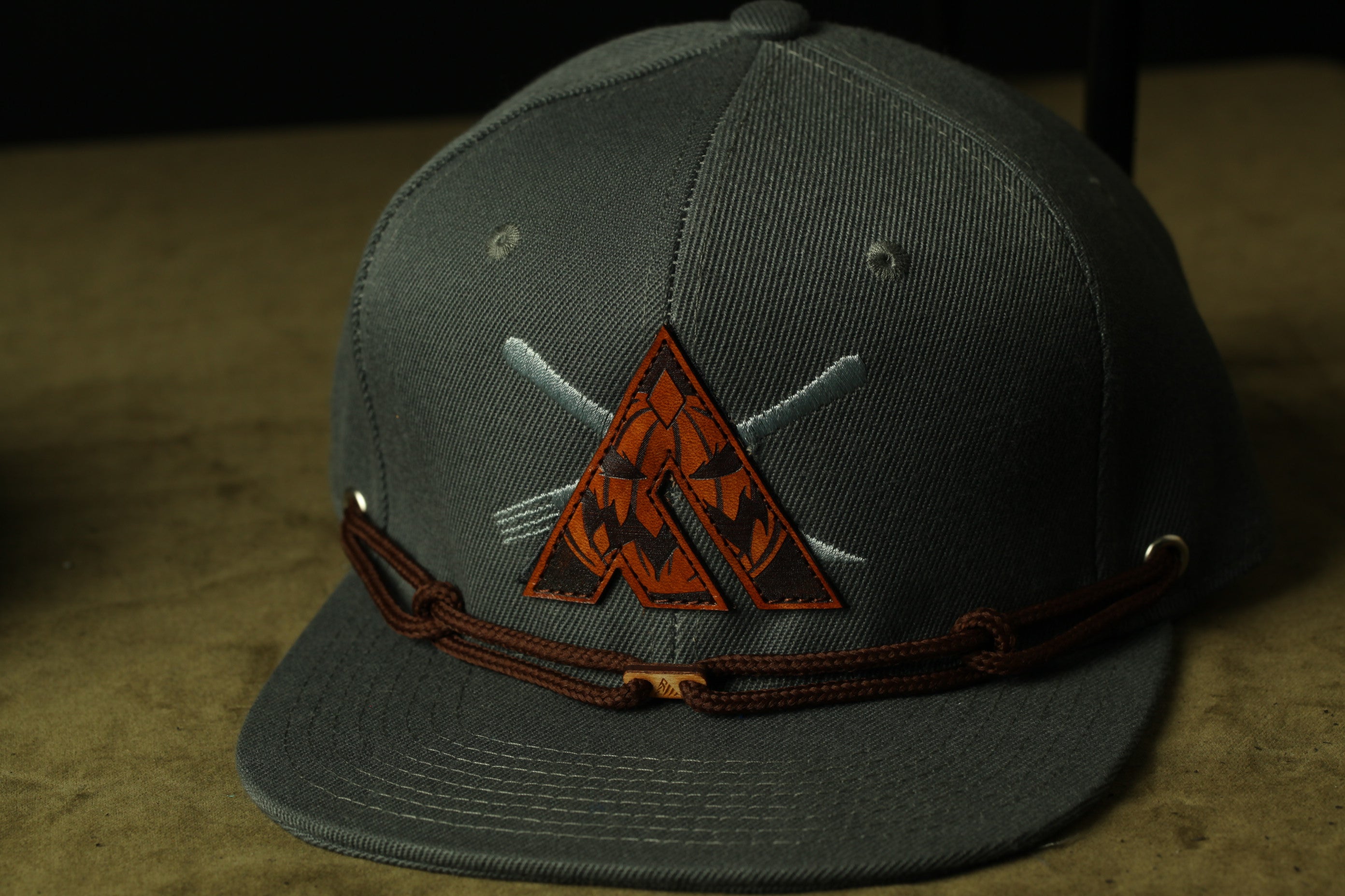 A gray baseball cap with a brown leather strap and a pumpkin-themed patch on the front.