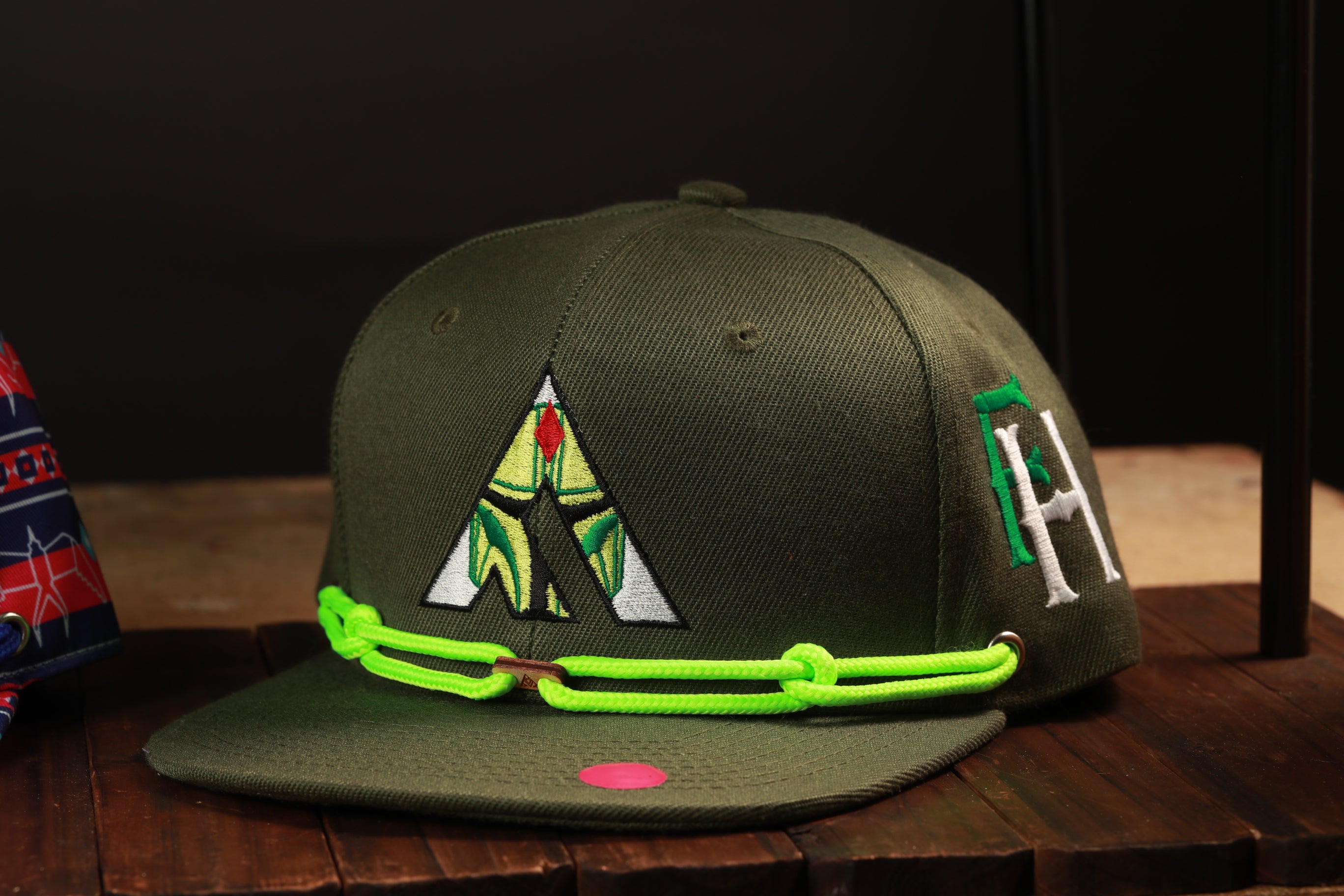 A green baseball cap with a unique logo and neon green chain strap is displayed on a wooden surface.
