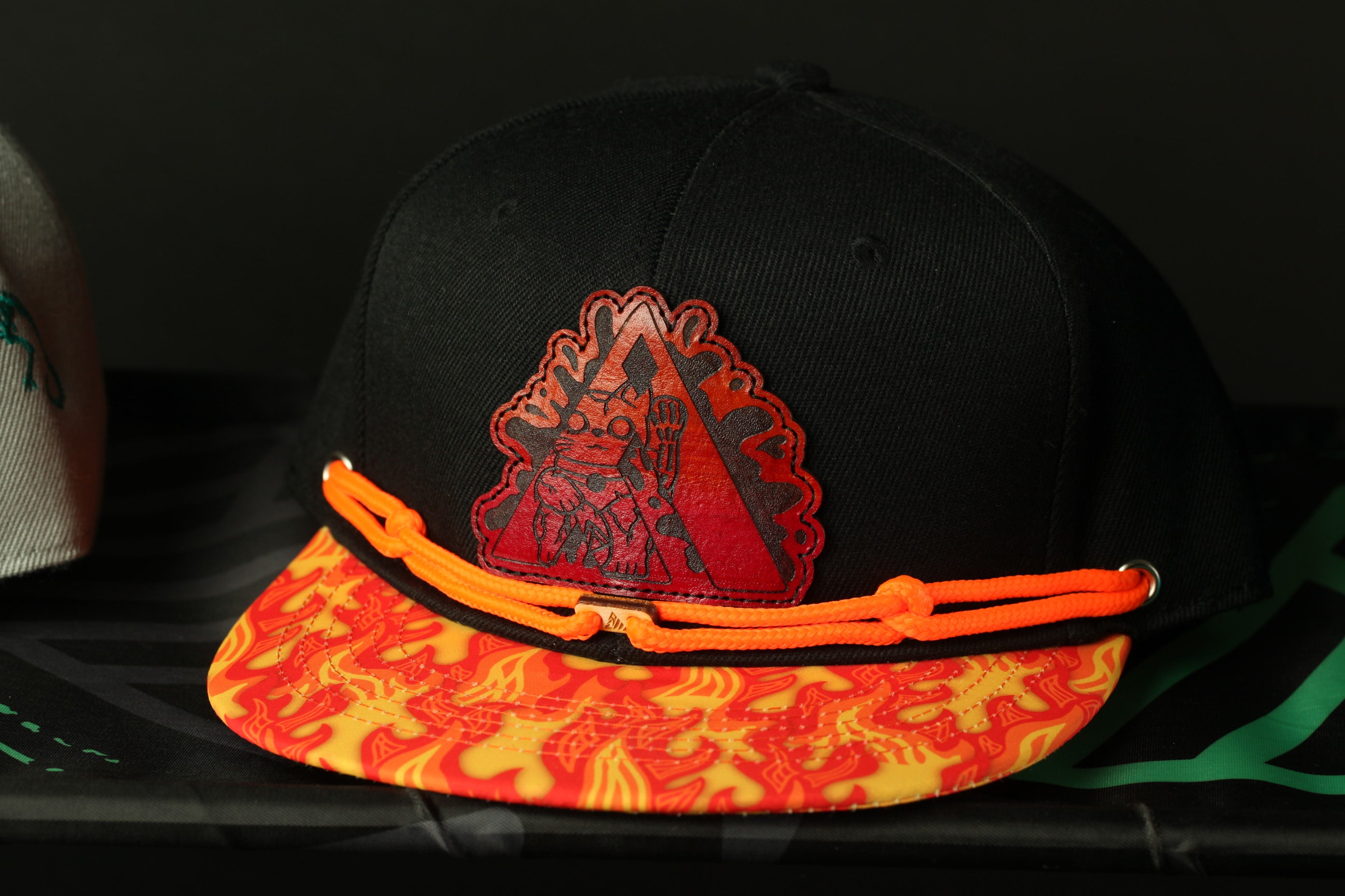 A black baseball cap with a red and orange patterned brim and a graphic design on the front.