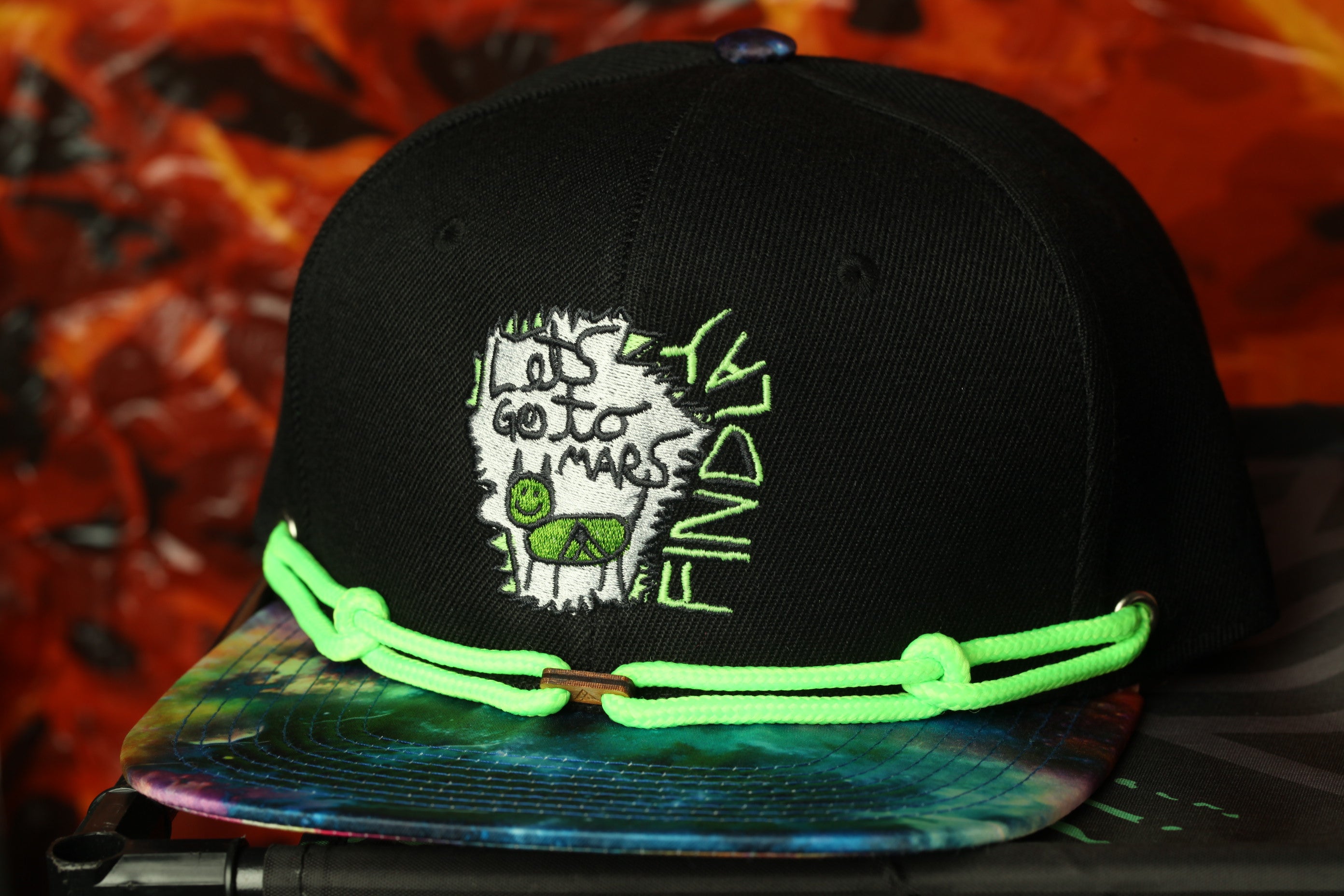 A black baseball cap with a colorful tie-dye pattern and neon green strings.