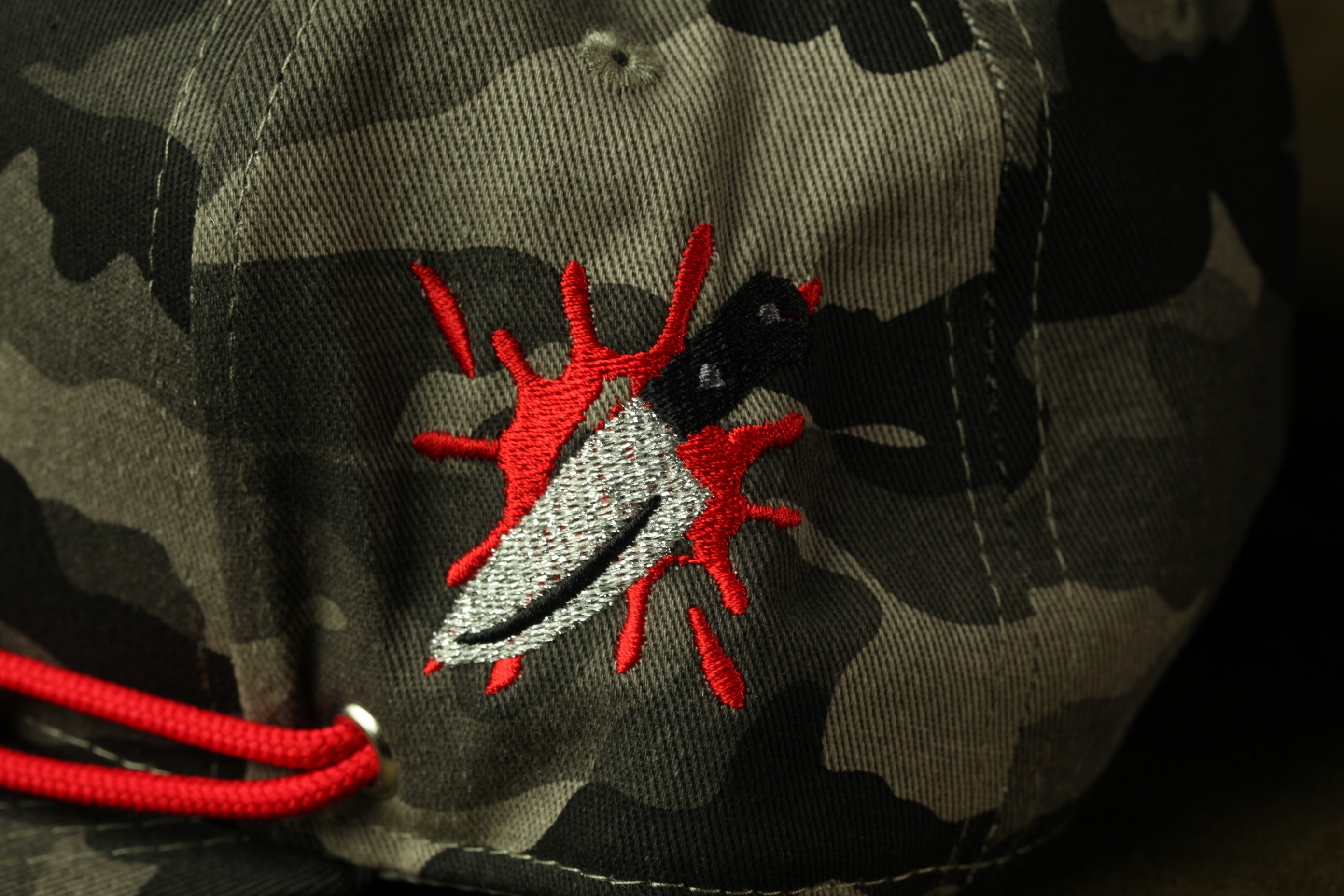 a close-up view of a camouflage-patterned fabric with a red and black embroidered knife design on it.