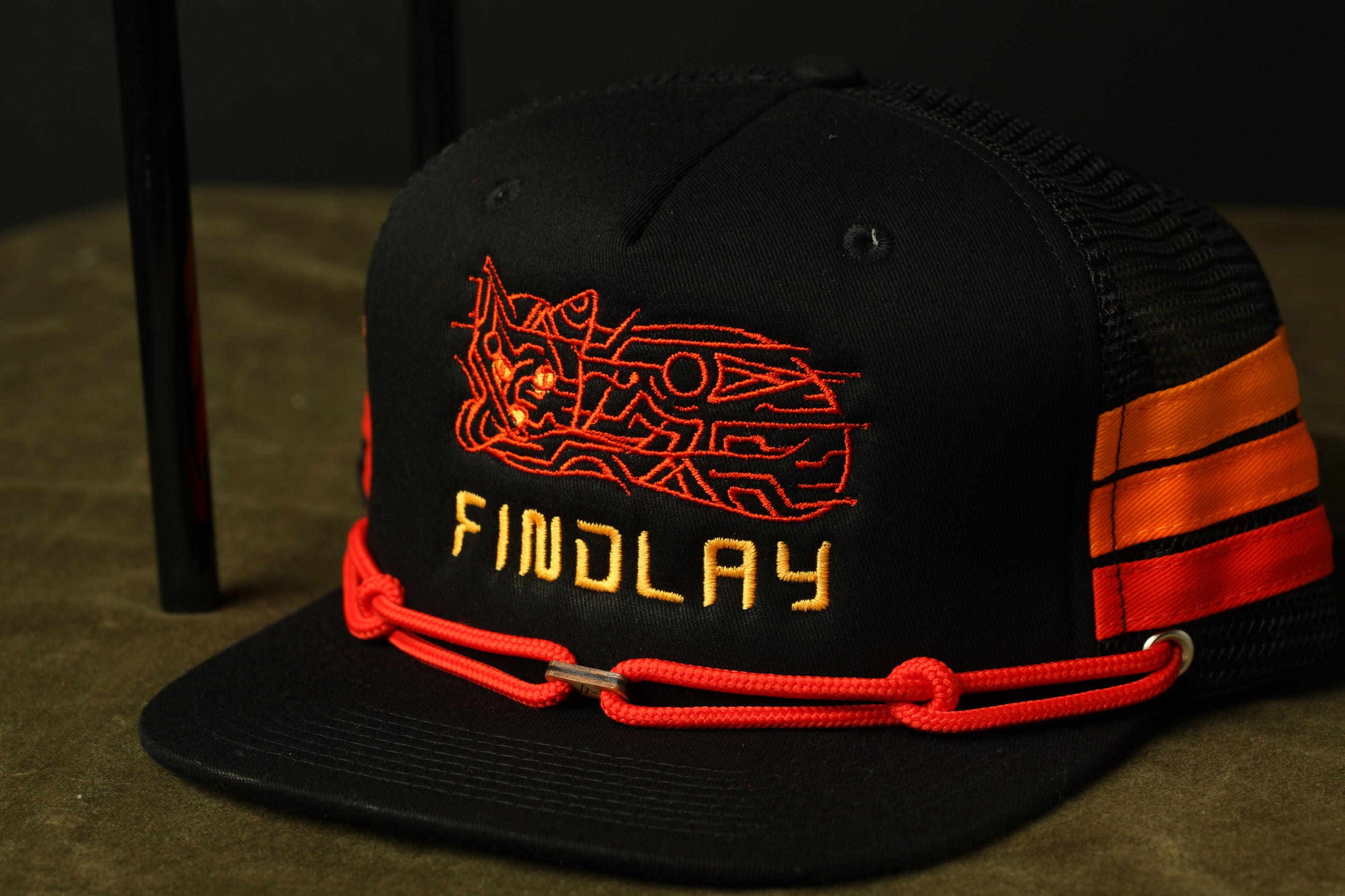 A black baseball cap with orange and red embroidered designs and the word "FINDLAY" printed on it.