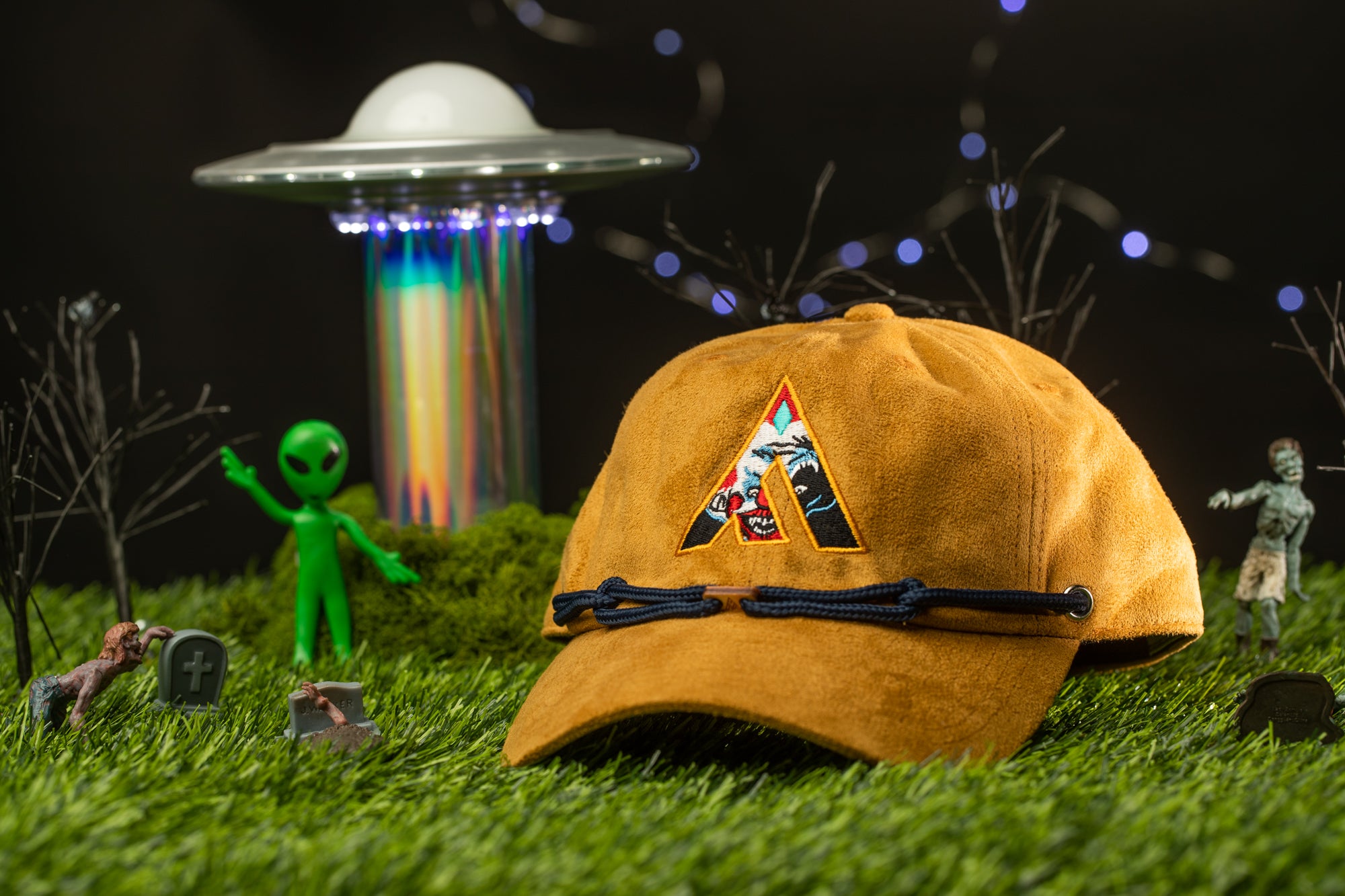 a green alien figurine, a brown baseball cap with a large "A" on it, and a small green alien figurine, all set against a dark background with a spaceship and a skull-like object.