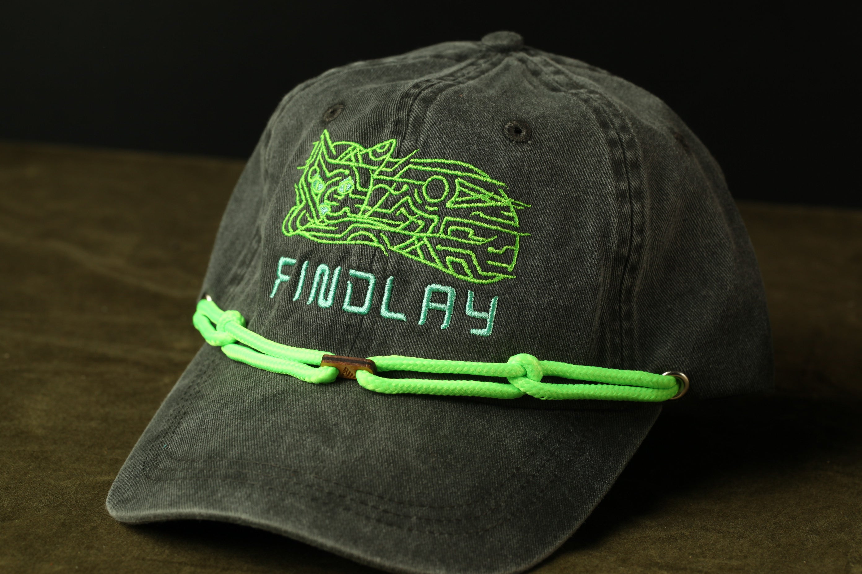 A black baseball cap with a green embroidered logo and the word "FINDLAY" printed on it.