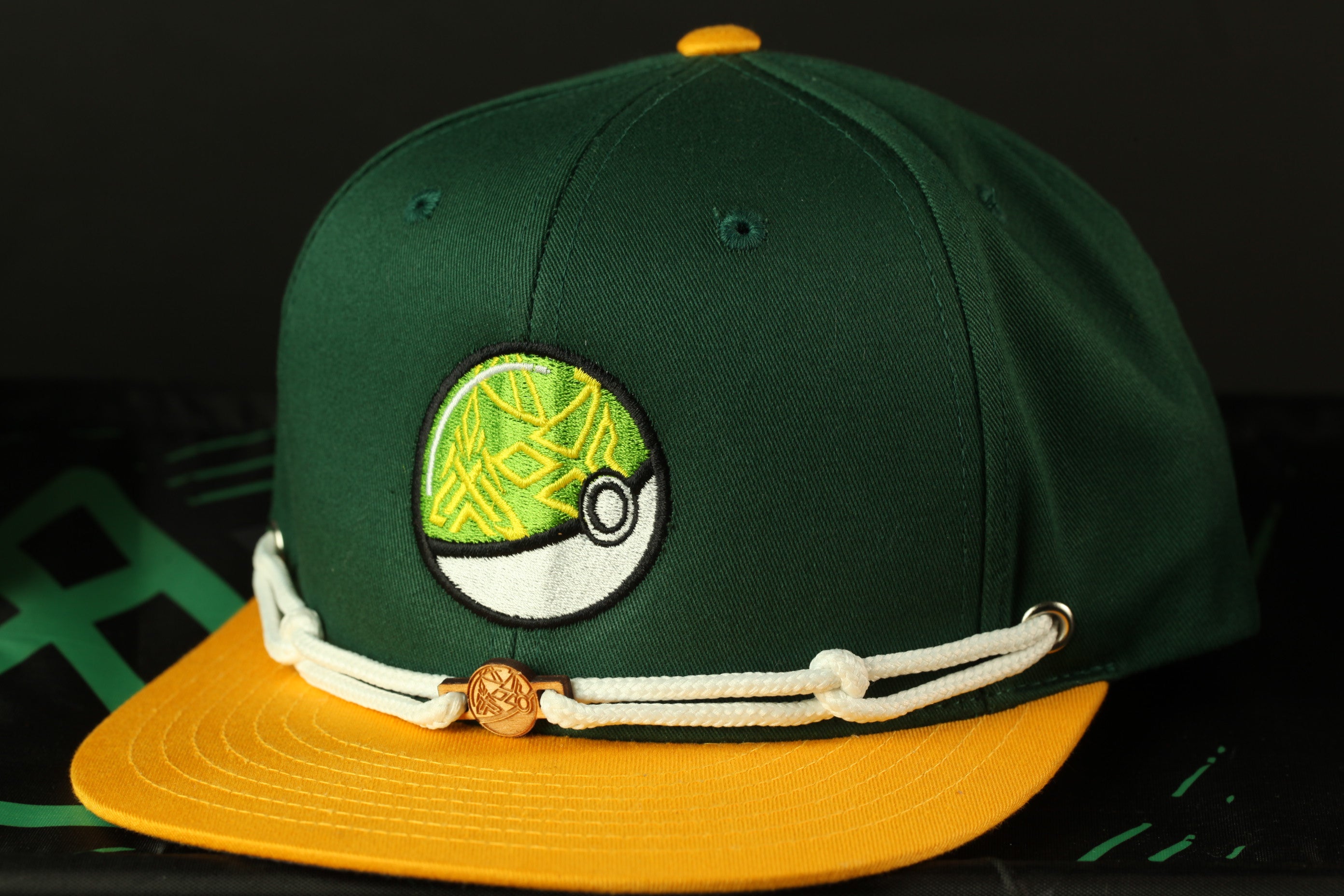 A green baseball cap with a yellow brim and a distinctive Pokemon-inspired design on the front.