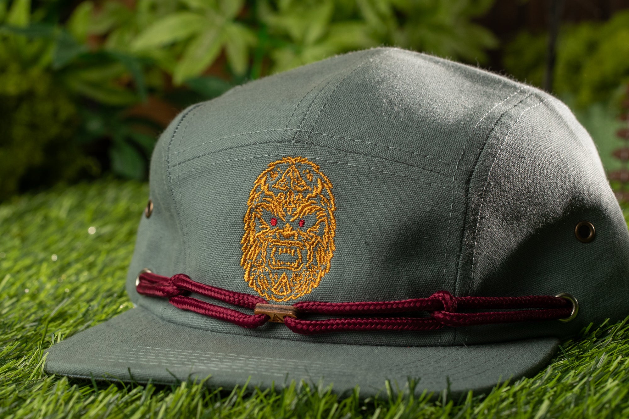 A gray baseball cap with a red band and an embroidered design on the front, placed on a grassy surface.