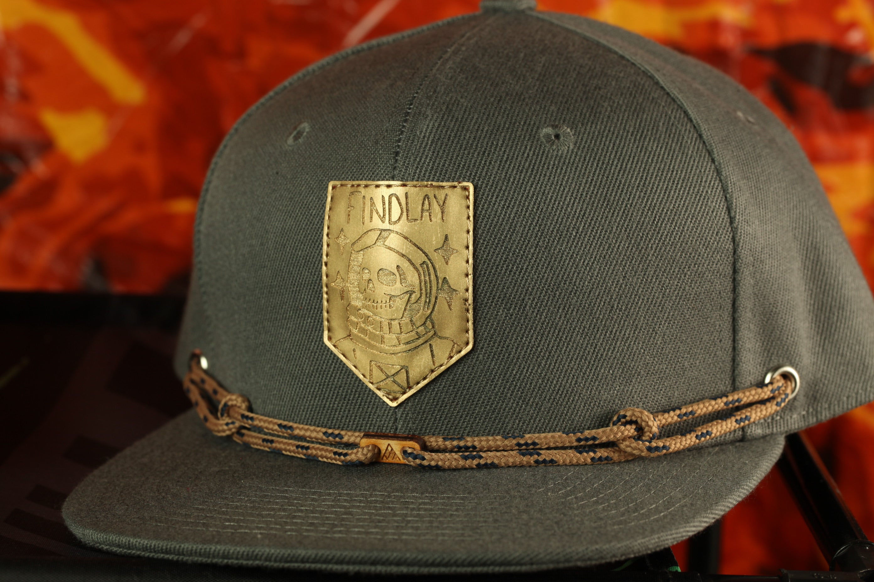 A dark green baseball cap with a gold patch on the front, featuring a skull and crossbones design.