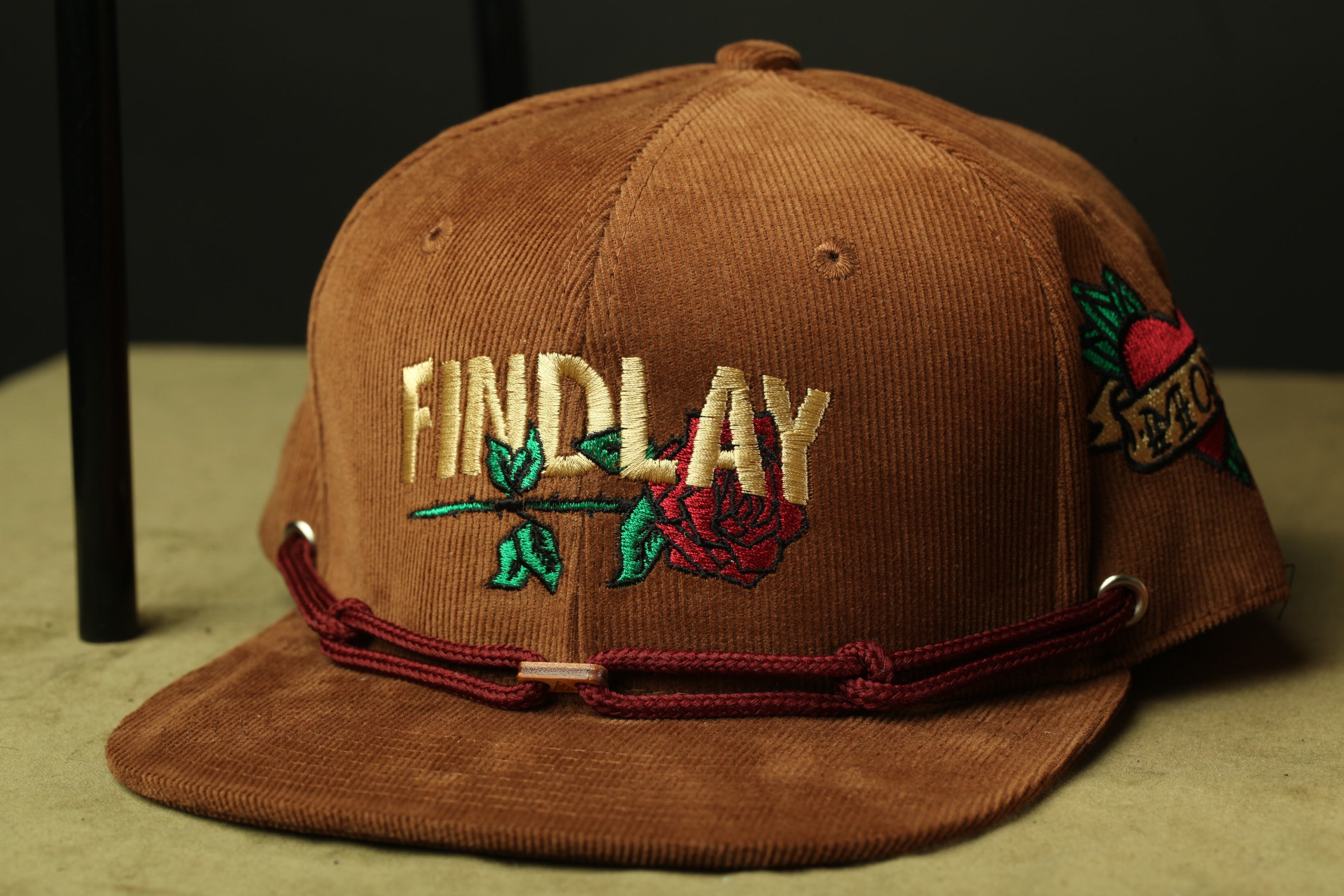 A brown baseball cap with embroidered text and a rose design.