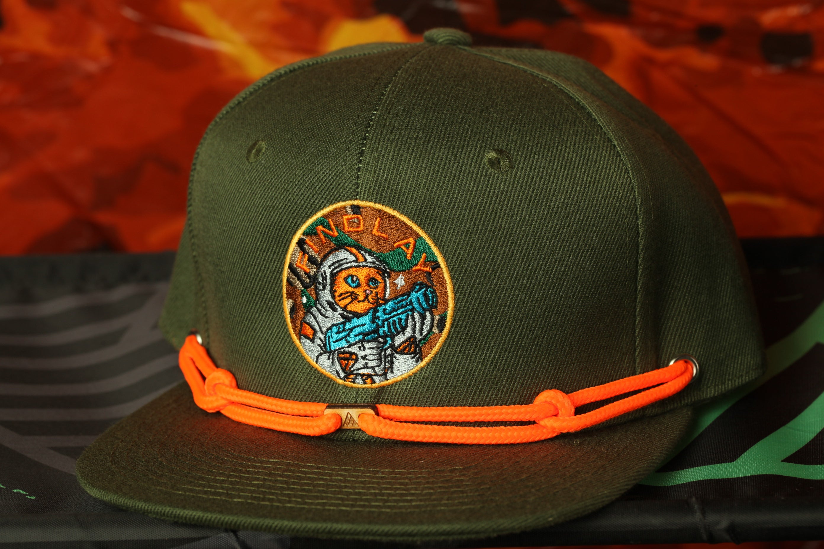 A green baseball cap with an orange chain strap and a circular patch featuring a cartoon character.