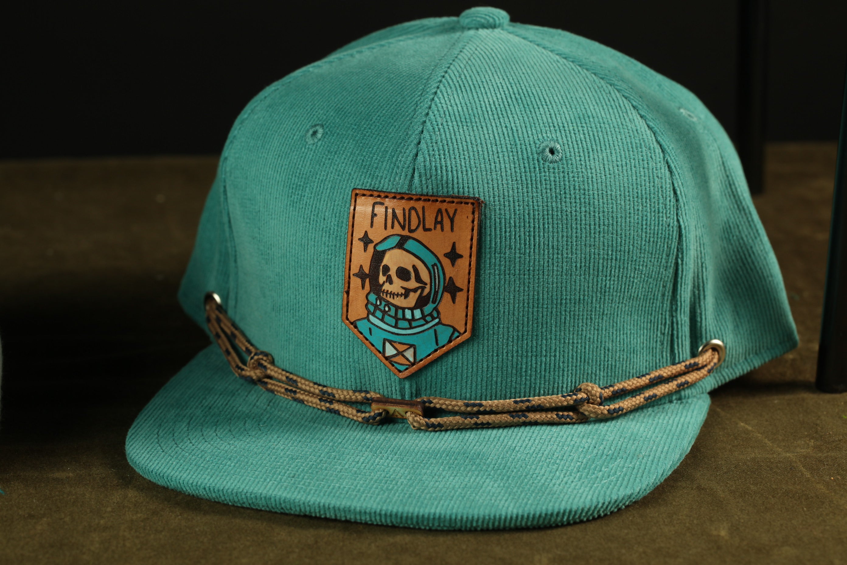 A turquoise baseball cap with a patch featuring a skull and the text "FINDLAY" on it.