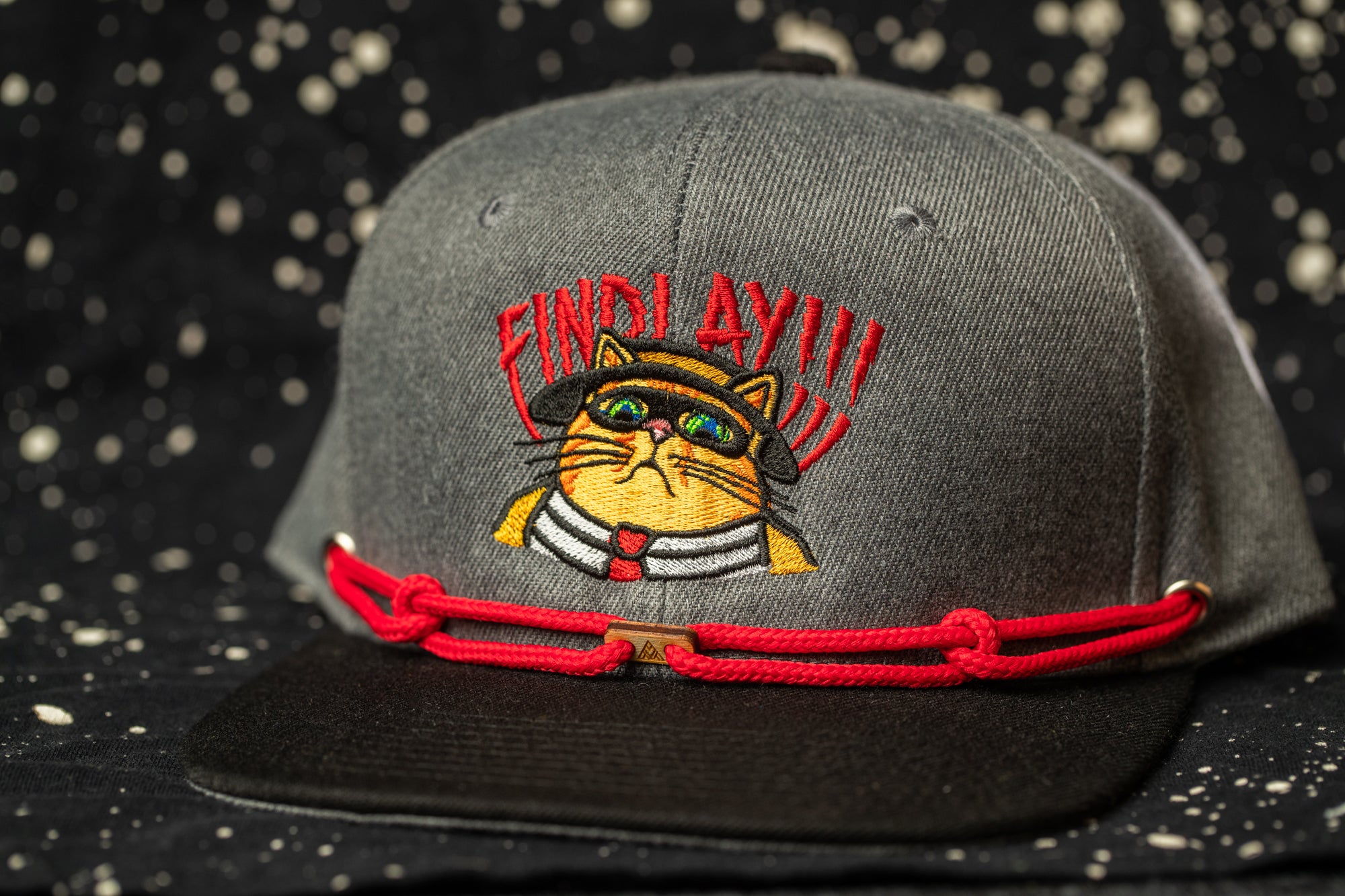 A gray baseball cap with a cat embroidered on it, wearing a red bandana and a red hat with a cat face.