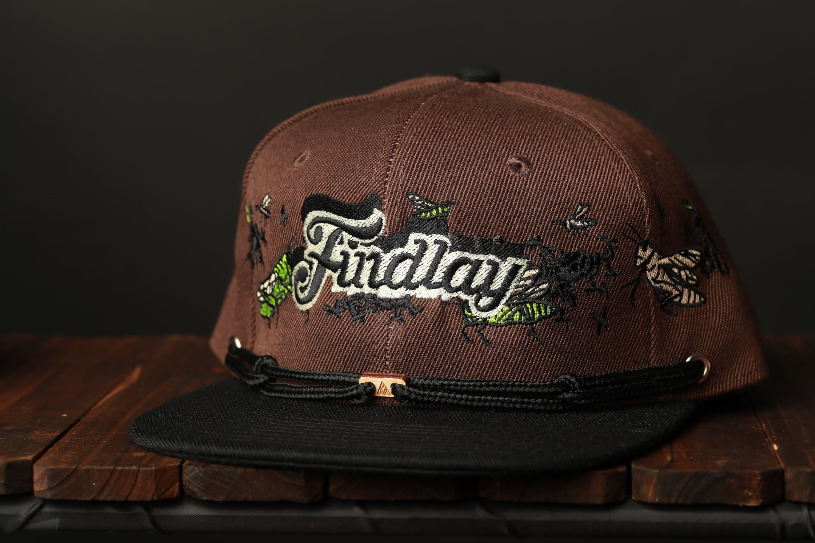 A brown baseball cap with the word "Findlay" embroidered on it, sitting on a wooden surface.