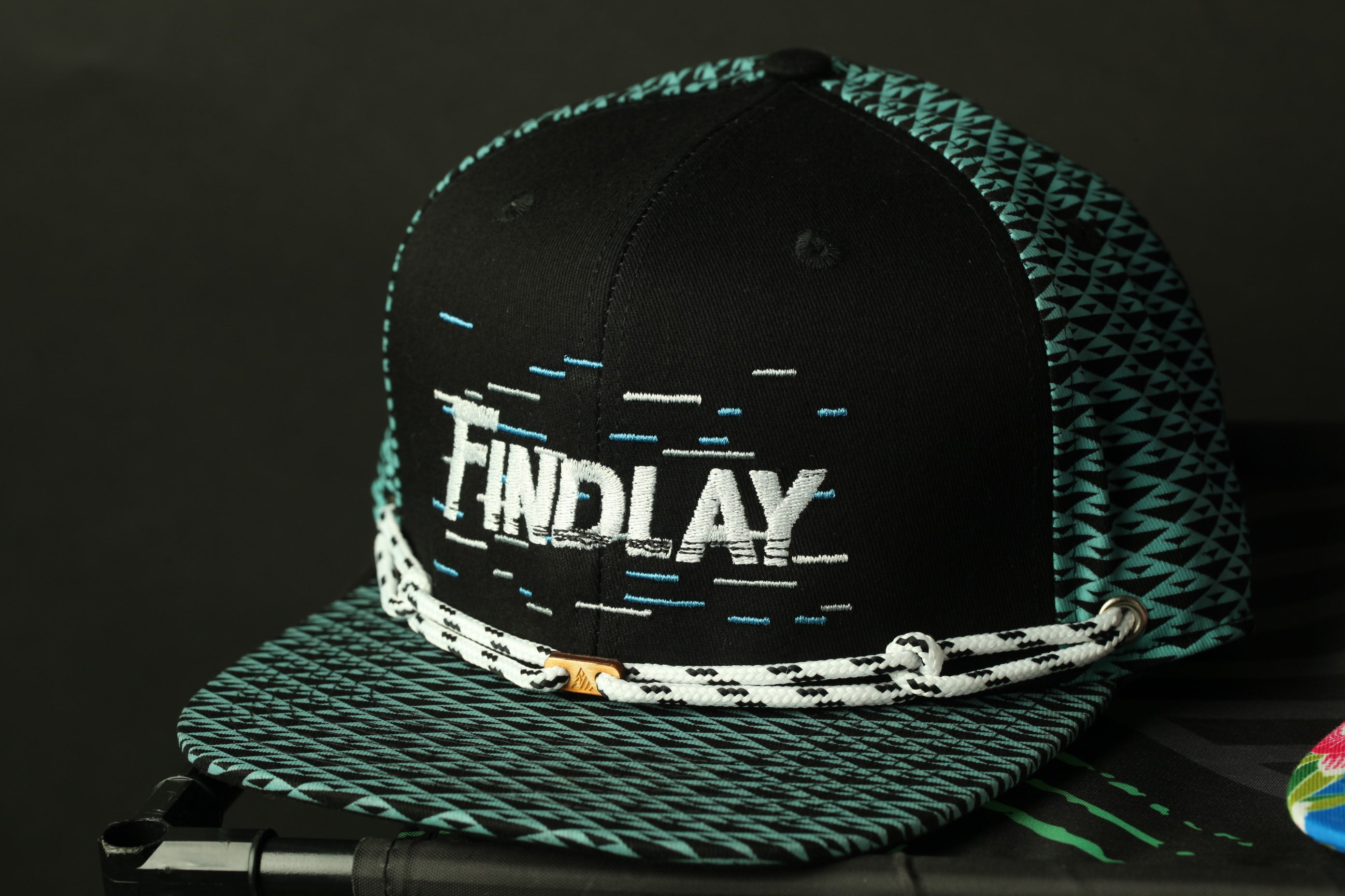 A black and teal patterned baseball cap with the word "FINDlay" printed on it.