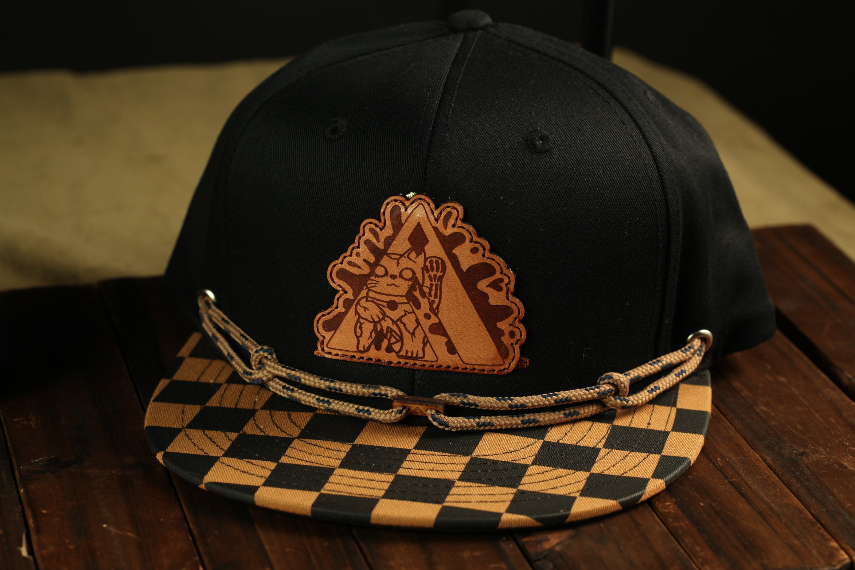 A black baseball cap with a checkered pattern and a leather patch featuring a cartoon character on the front.