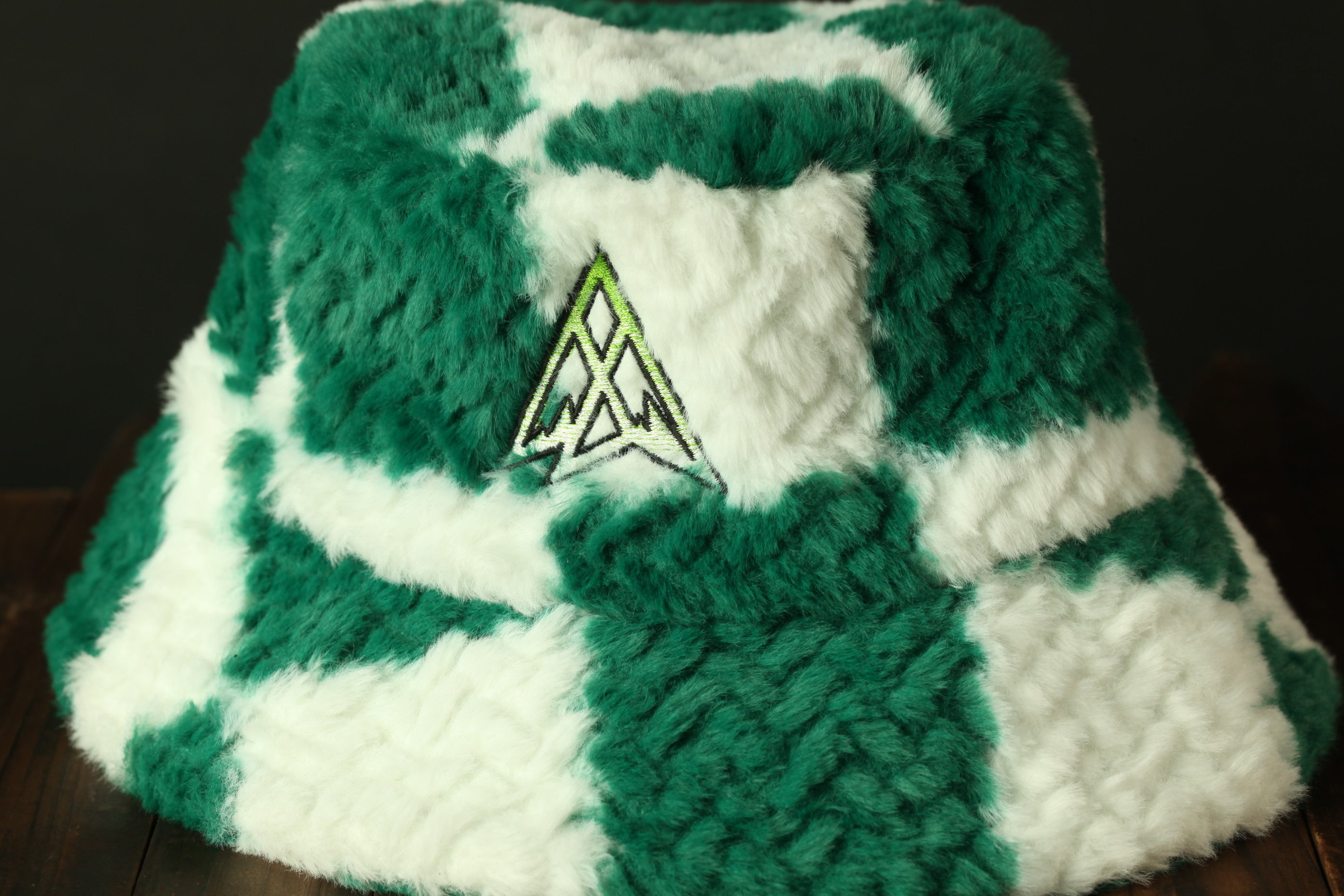 A close-up image of a green and white checkered bucket hat with a distinctive triangle-shaped logo on the front.