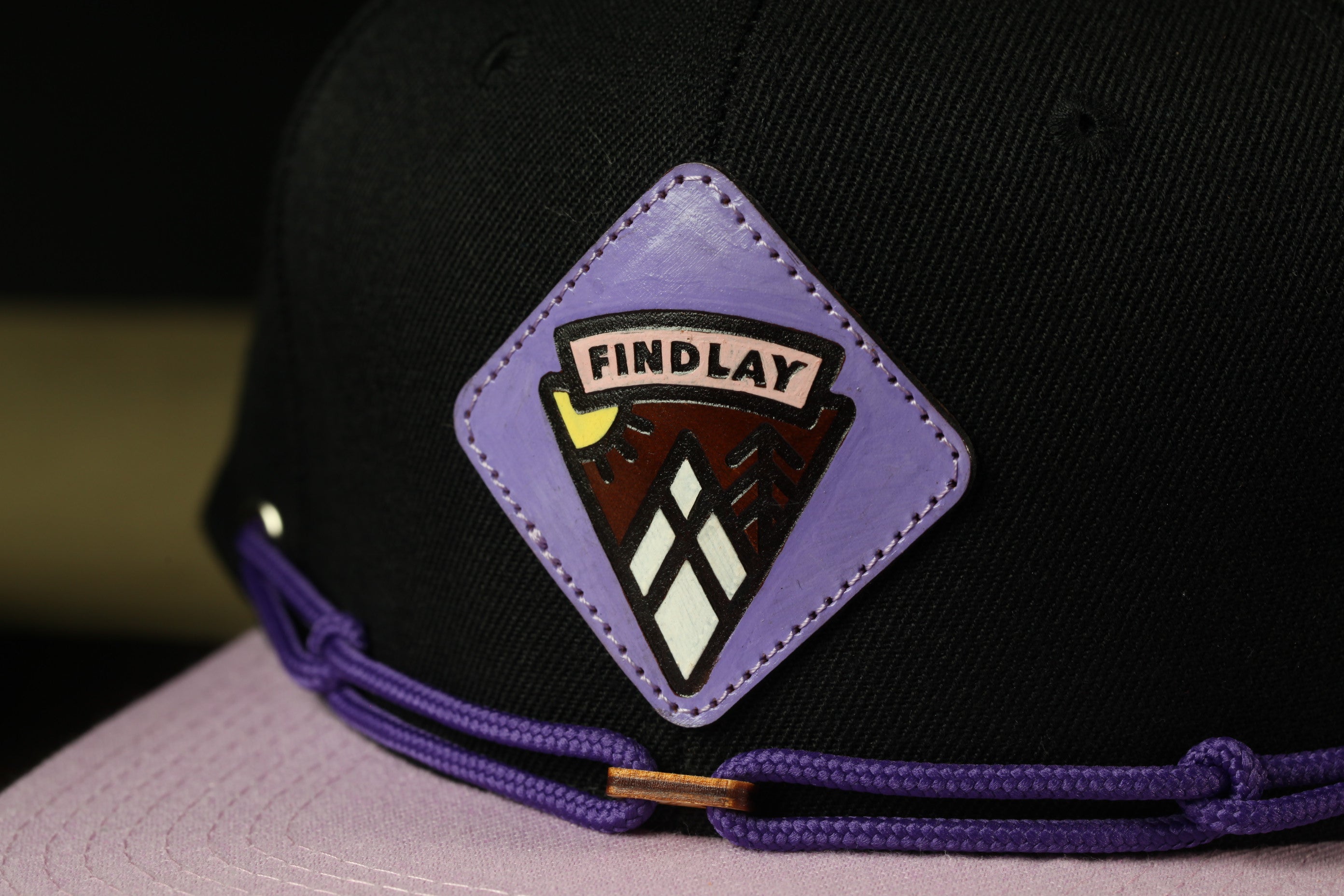 A close-up view of a black baseball cap with a purple and white logo on the front.
