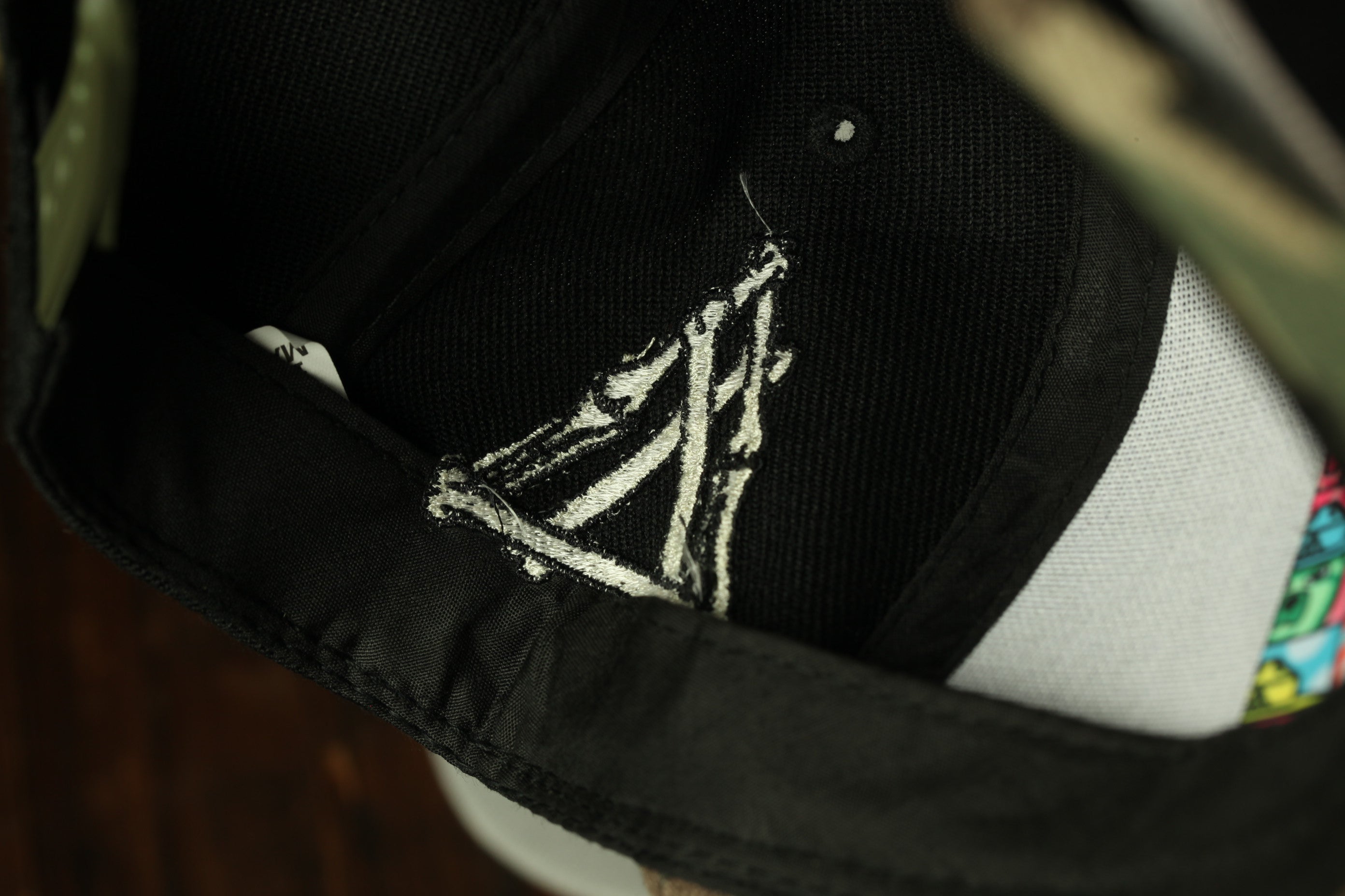 a close-up view of a black baseball cap with a white embroidered design on the front.
