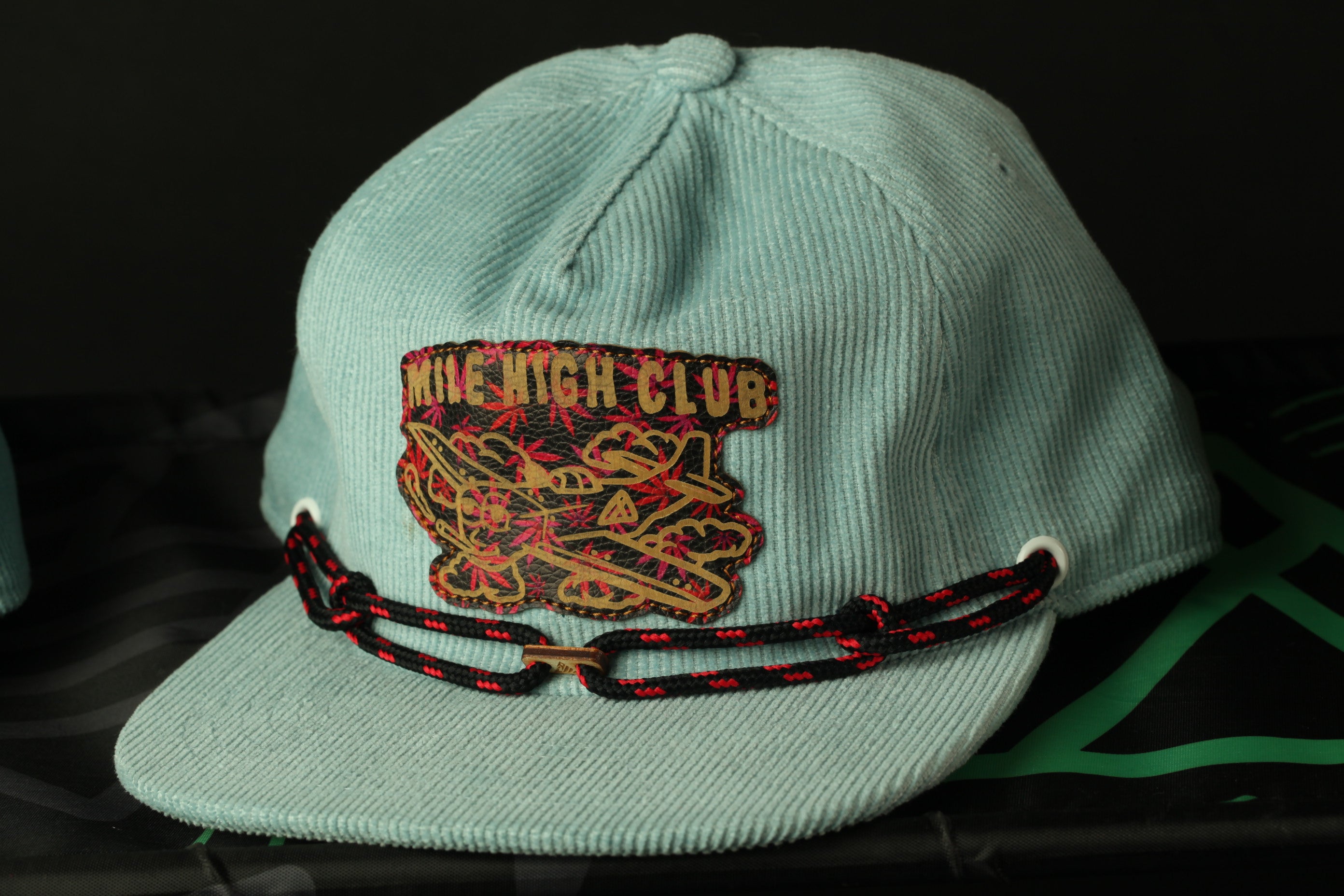 A light blue baseball cap with a patch on the front, featuring a graphic design and the text "MILE HIGHL CLUB".