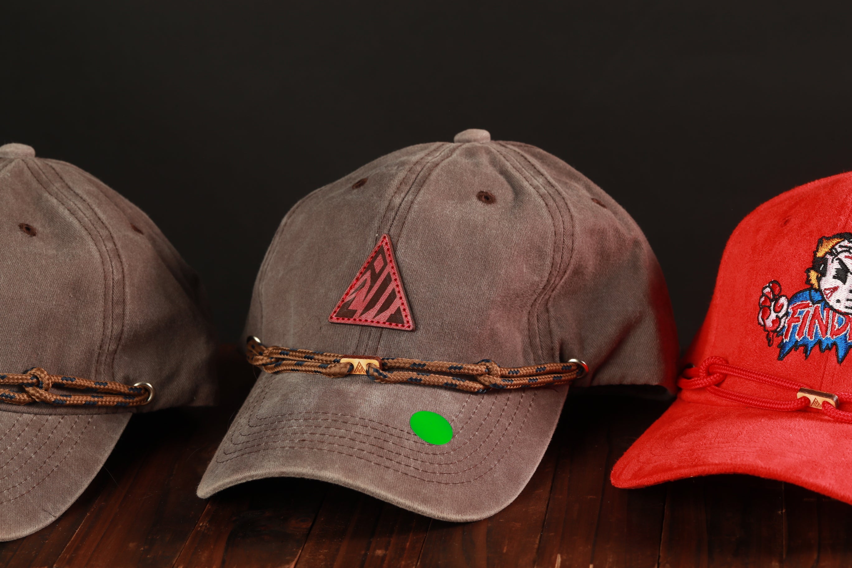 Three baseball caps are displayed on a wooden surface, with two gray caps and one red cap.