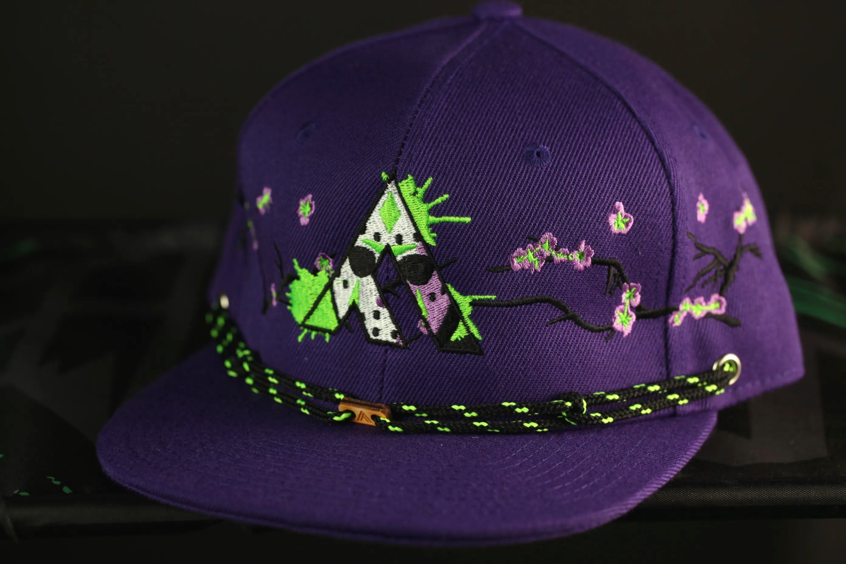A purple baseball cap with a green and white geometric design and floral accents.
