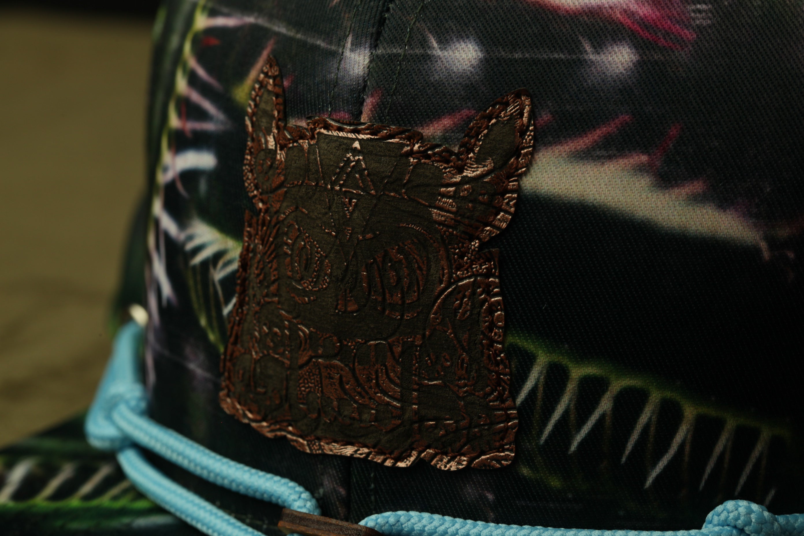A close-up view of a dark-colored hat with a brown leather patch featuring an intricate design on the front.