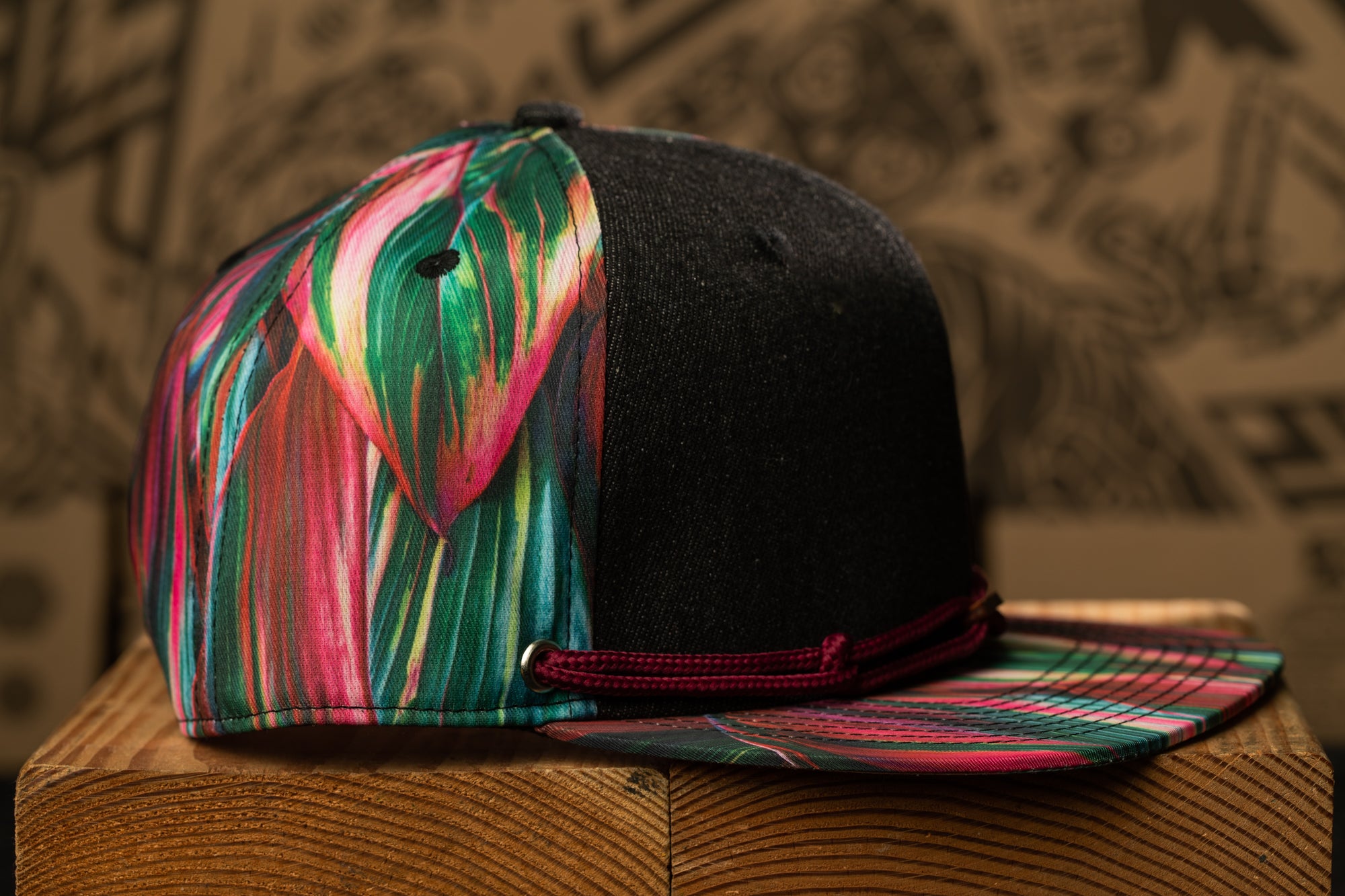 A colorful, patterned baseball cap with a black brim and a red band around the base rests on a wooden surface.