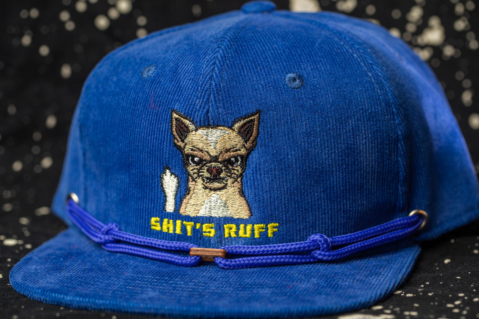 A blue baseball cap with a cartoon image of a dog and the text "SHIT'S RUFF" printed on it.