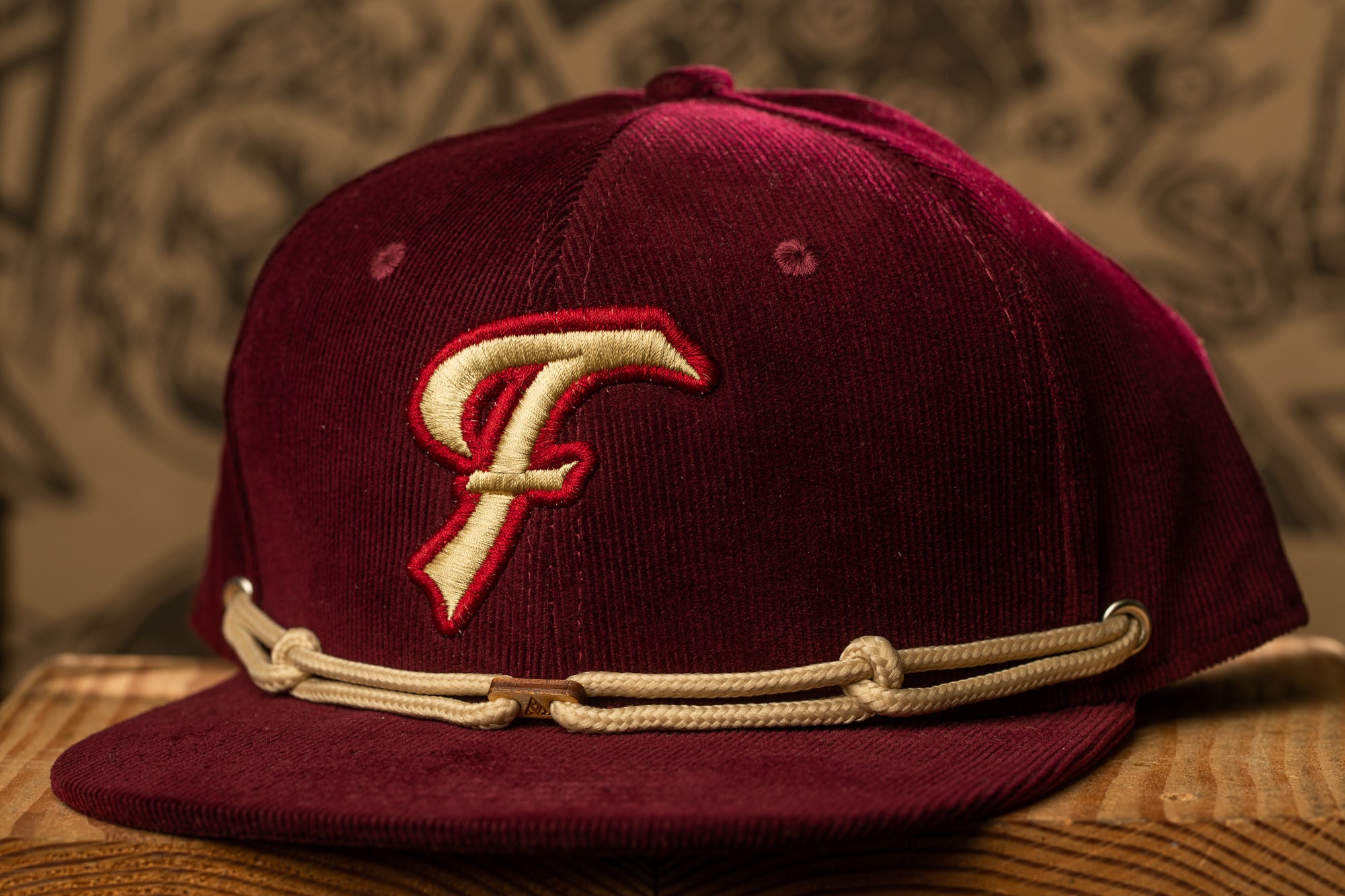 A burgundy baseball cap with a white "F" logo on the front, sitting on a wooden surface.