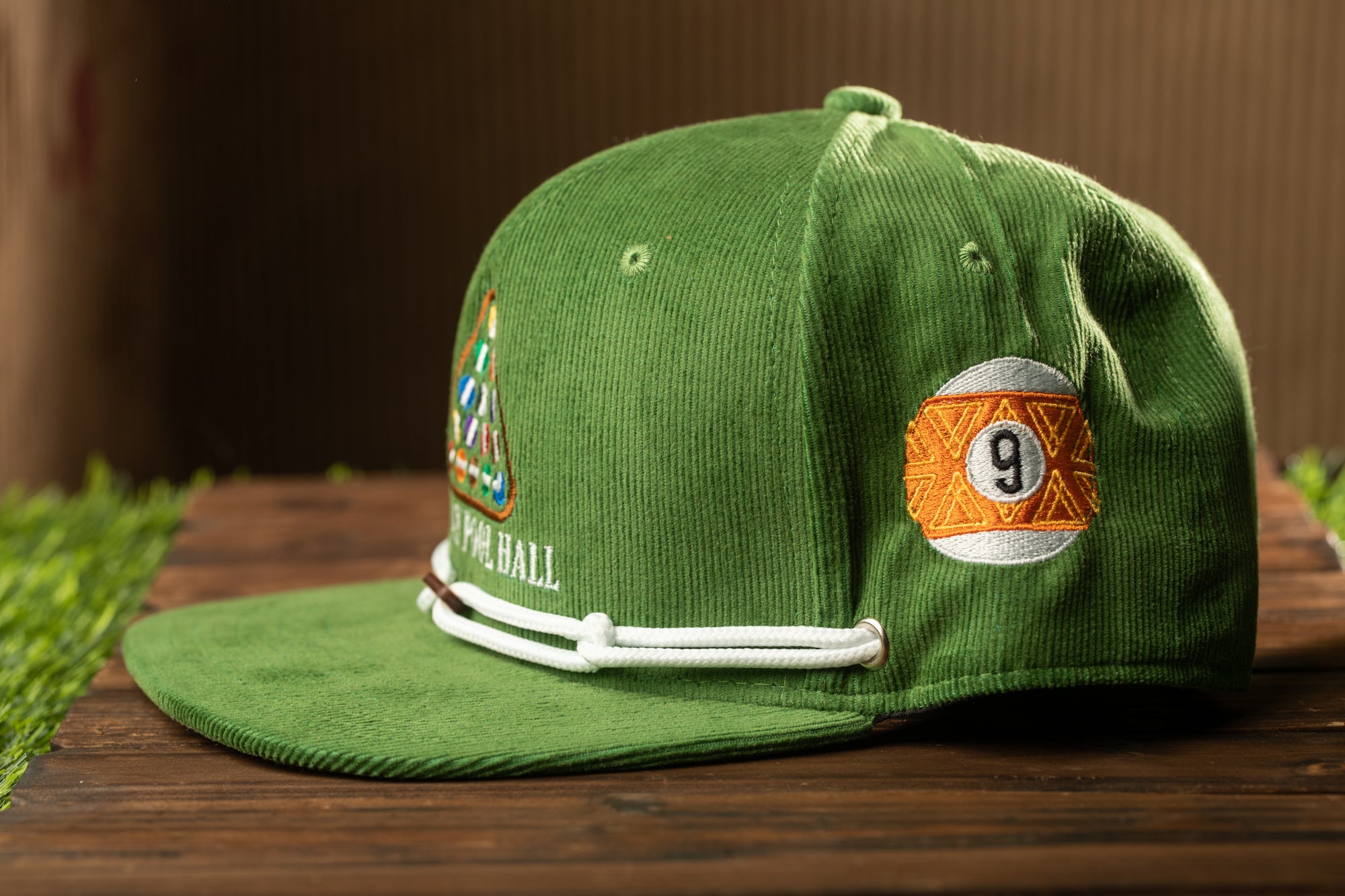 A green baseball cap with a pool ball patch and the number 9 on it, placed on a wooden surface.