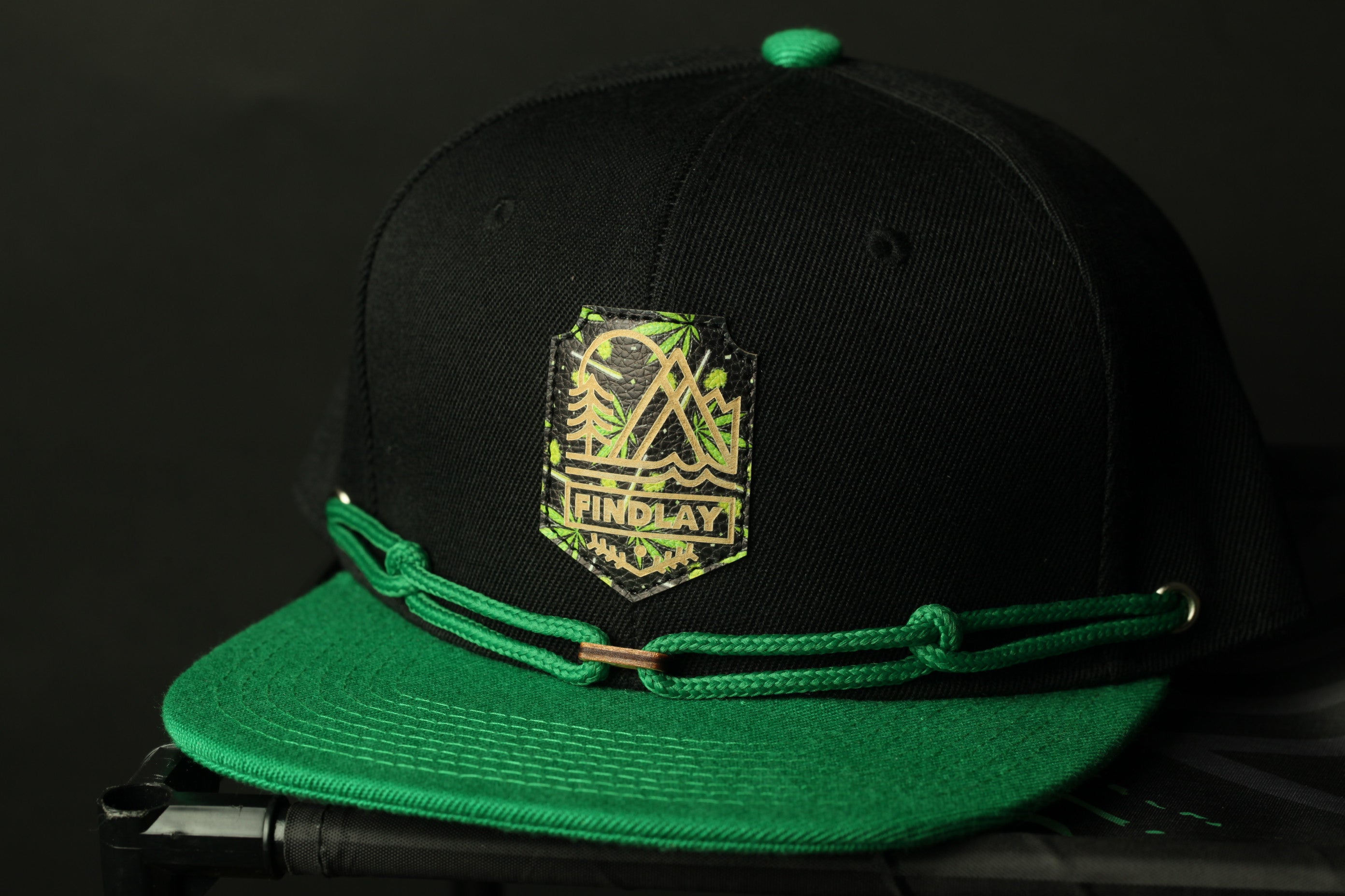 A black baseball cap with a green brim and a green-colored logo on the front.