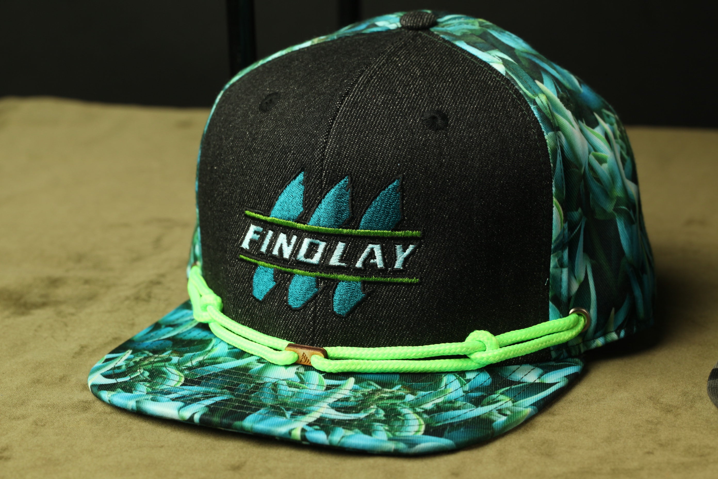 A black baseball cap with a tropical leaf pattern and the word "FINDlay" printed on it.