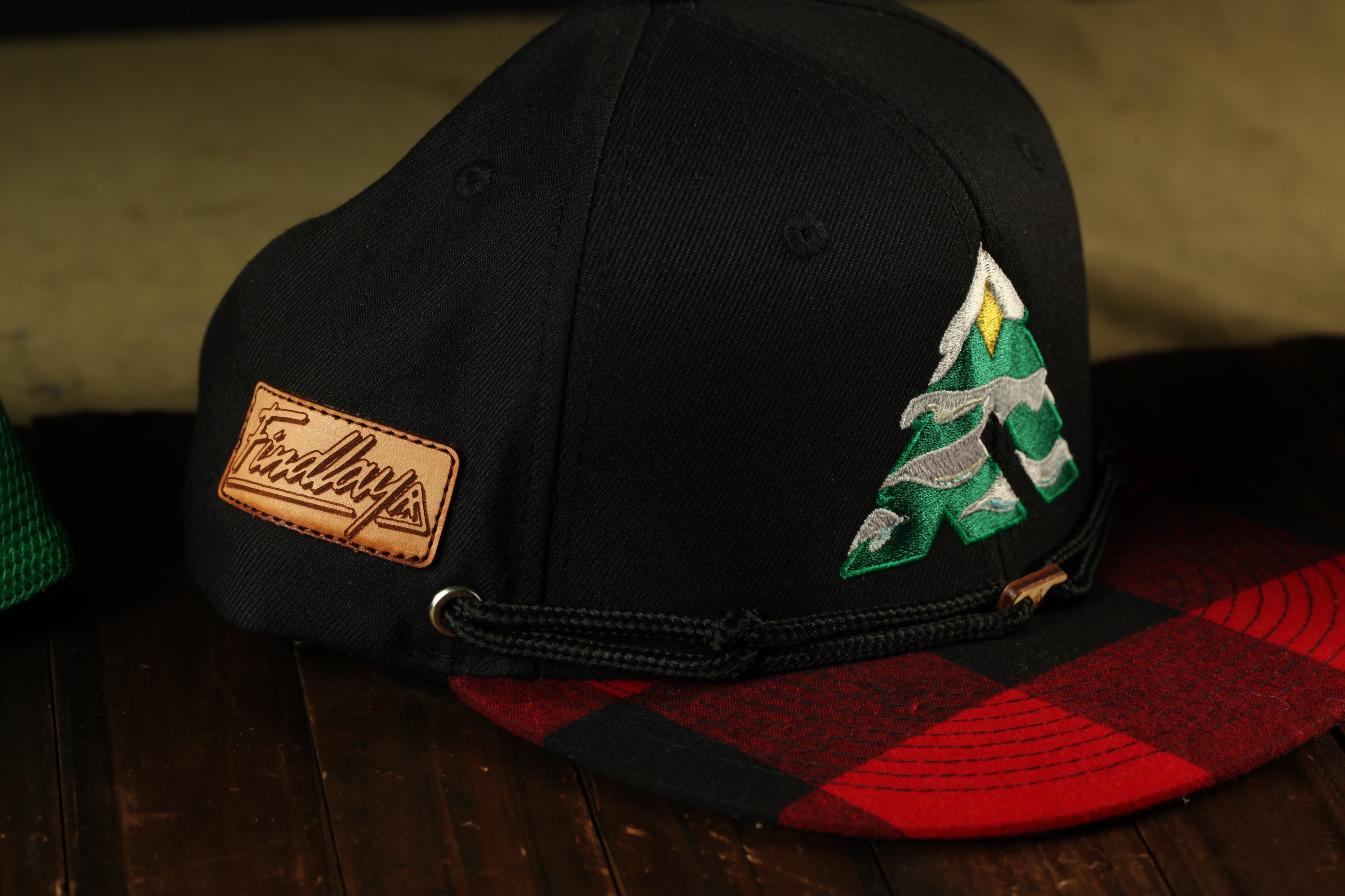 A black baseball cap with a plaid pattern and a small embroidered tree design on the front.