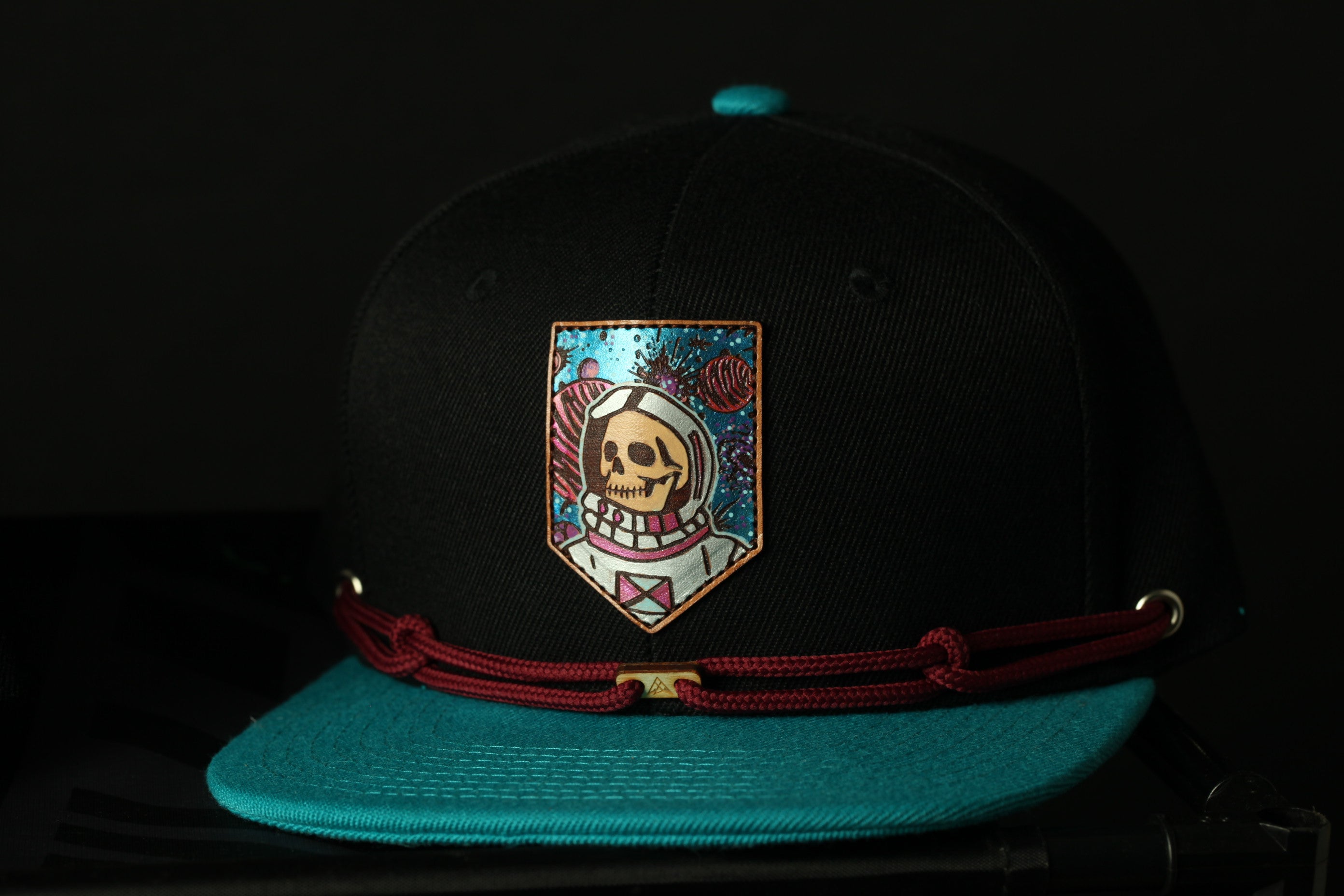 A black baseball cap with a colorful, artistic design on the front, including a skull and a space-themed motif.
