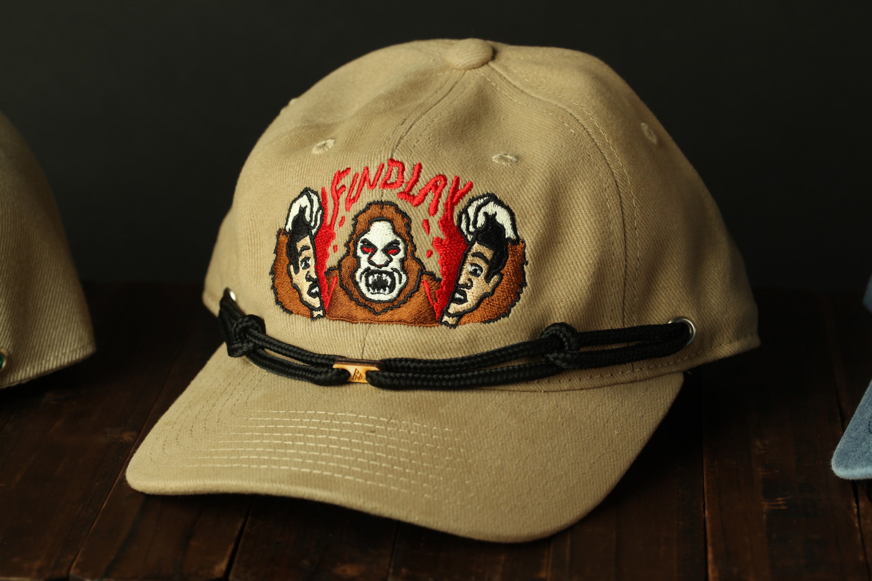 A beige baseball cap with a graphic design featuring a cartoon character and the word "FINDLAY" printed on it.