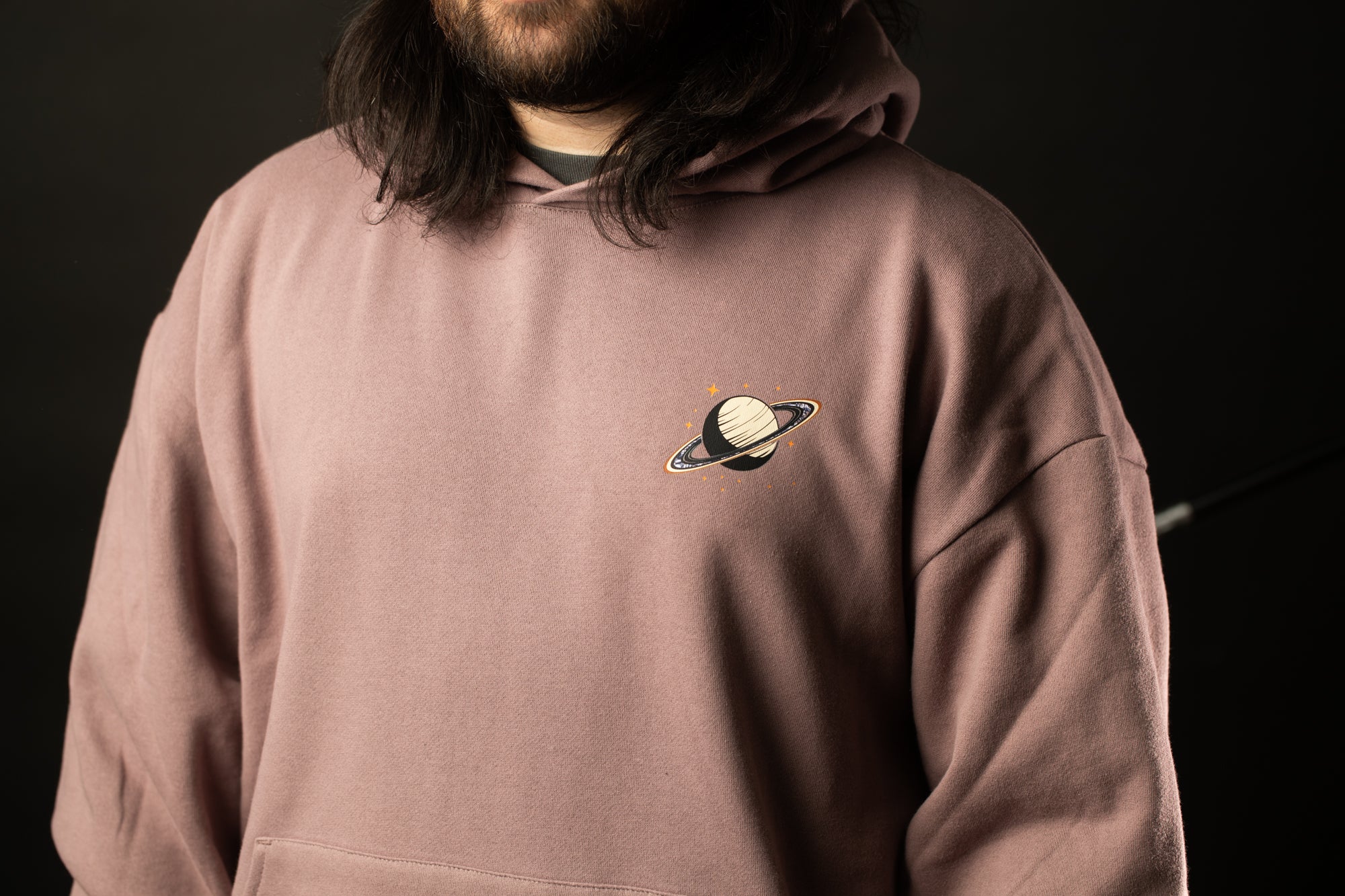 A person wearing a pink hoodie with a small planet design on the front.