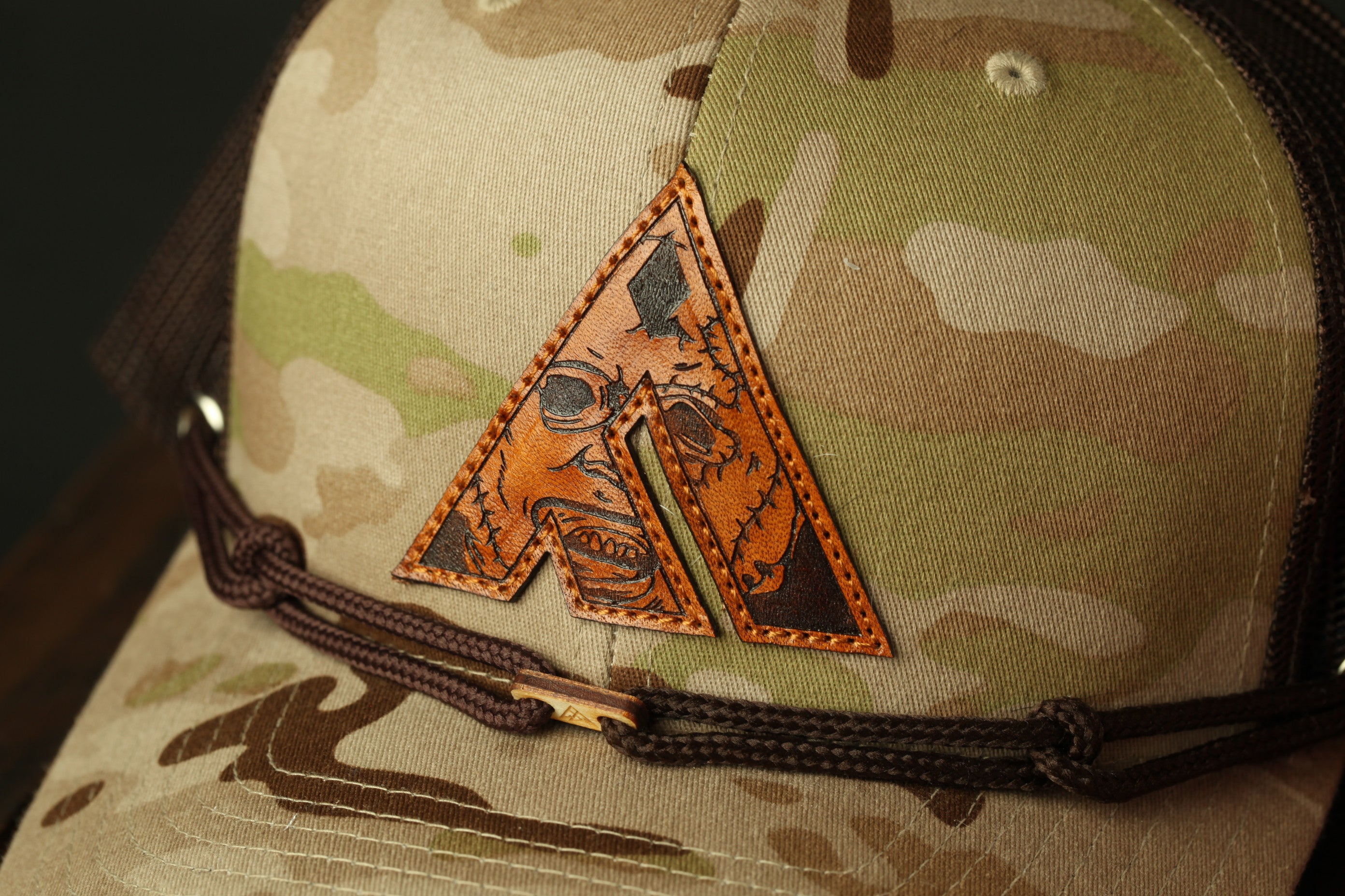 A close-up view of a camouflage-patterned baseball cap with a unique, hand-stitched letter "A" on the front.