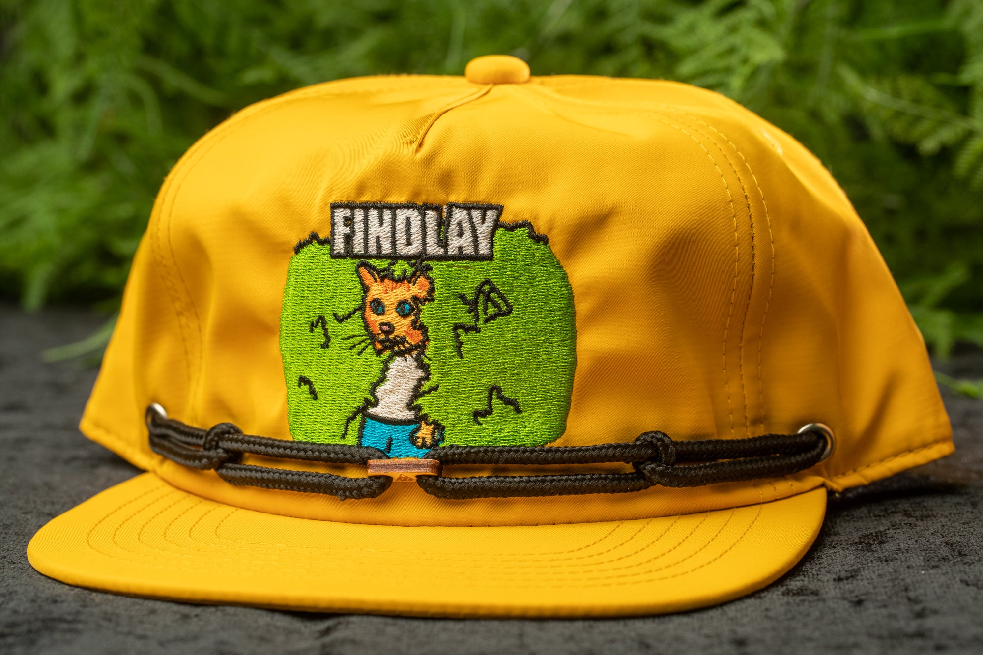 A yellow baseball cap with a cartoon cat design and the word "FINDOLAY" printed on it.