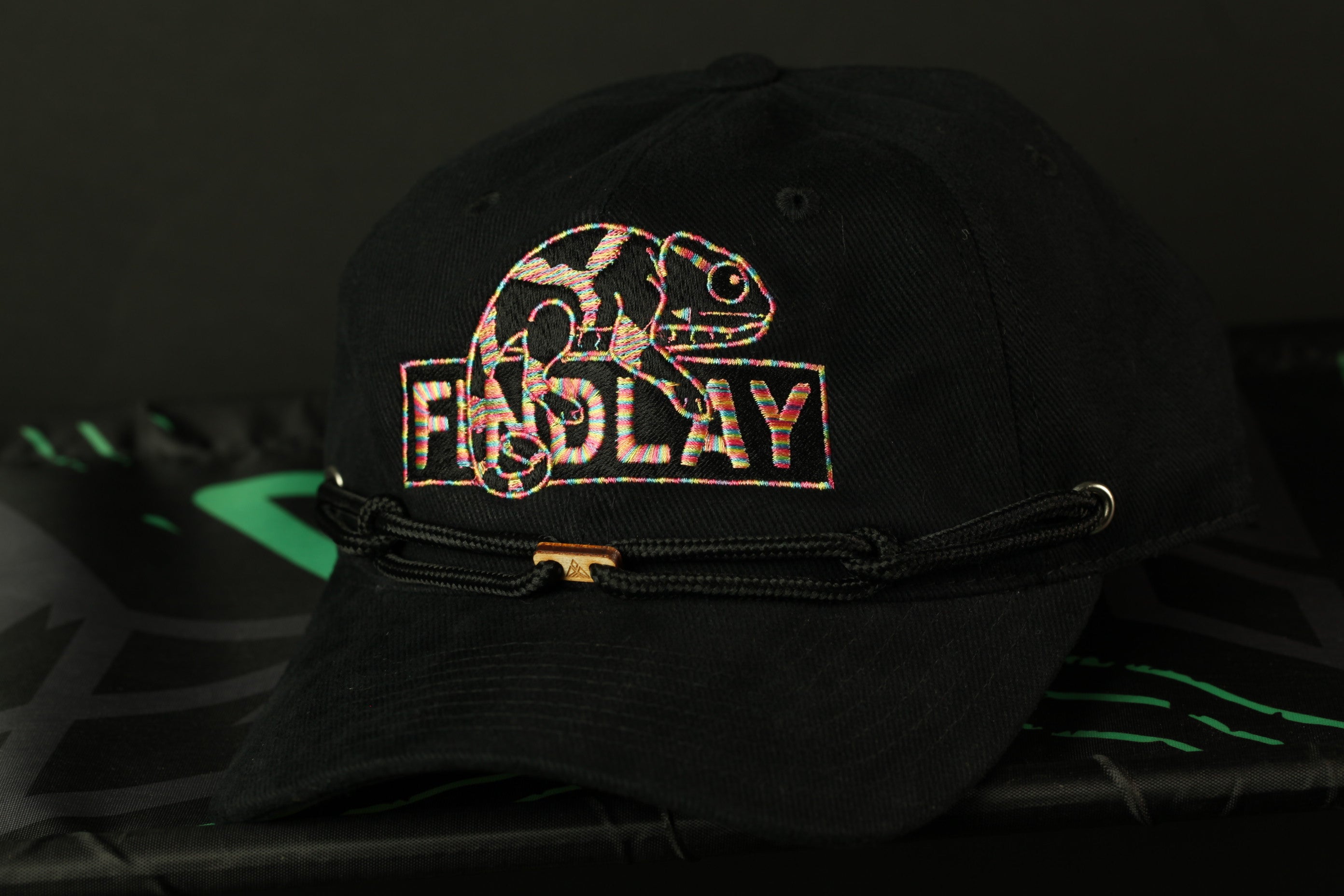 A black baseball cap with a colorful chameleon design and the word "FIDDLY" printed on it.