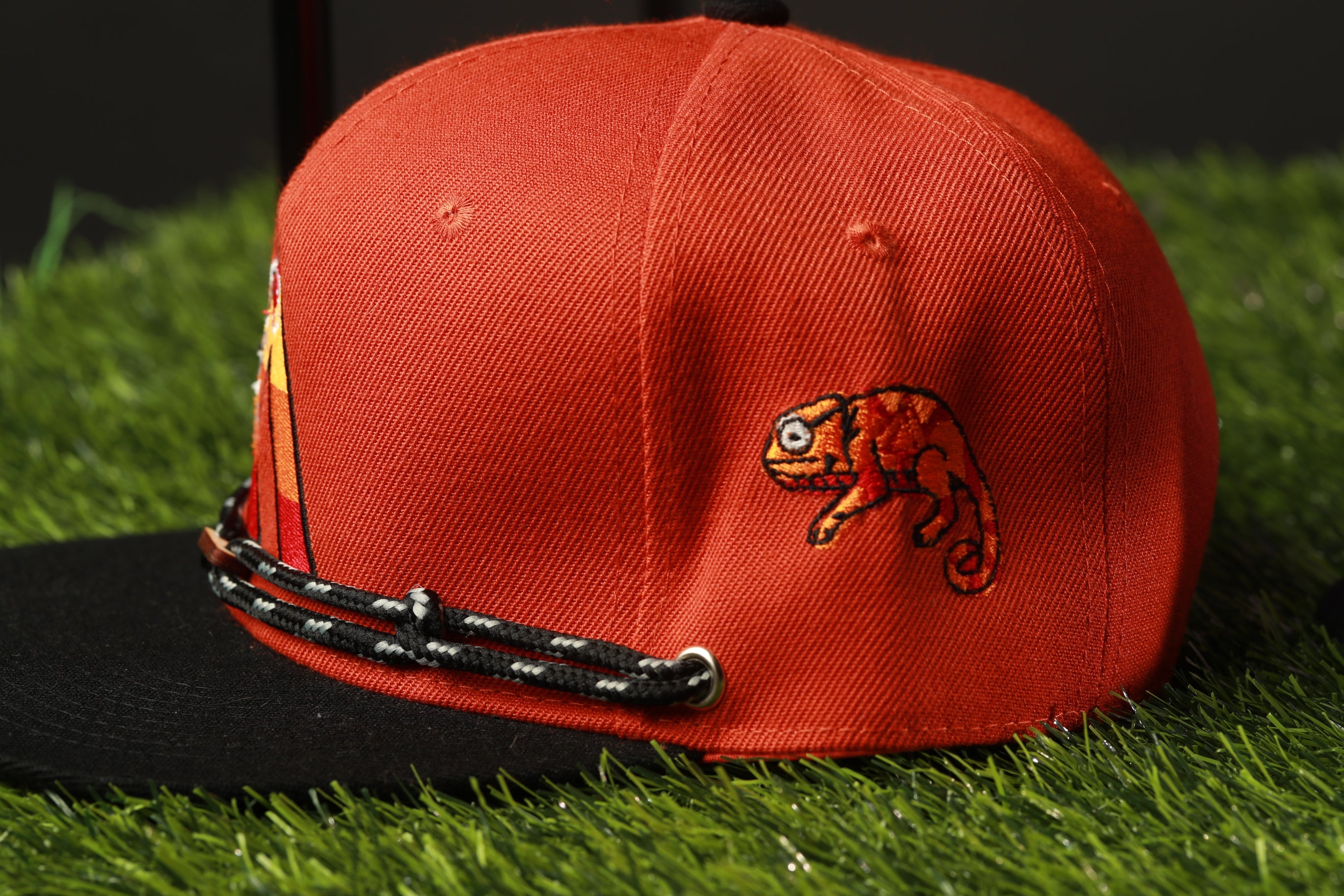 A red baseball cap with a chameleon design on the front, placed on a grassy surface.