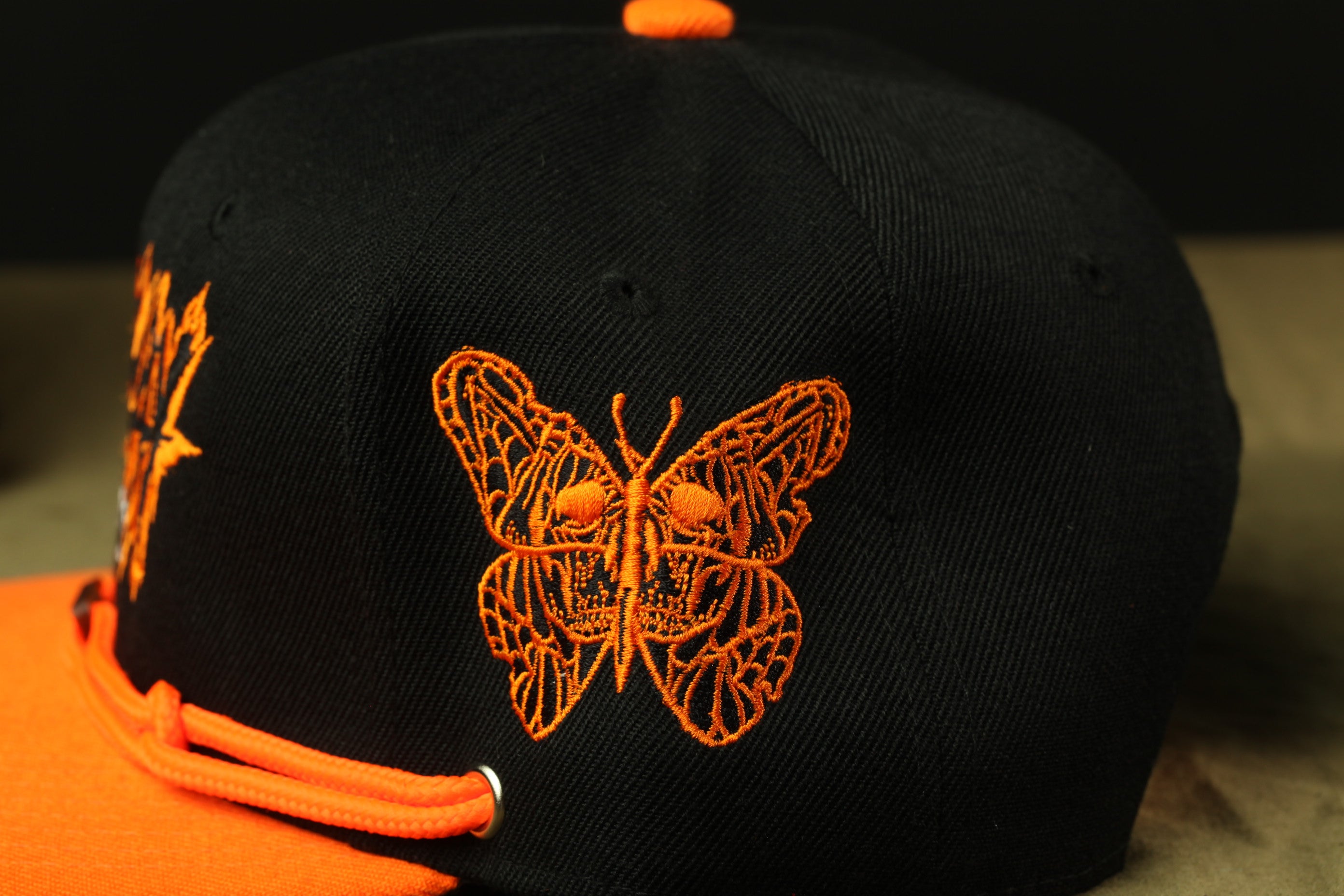 A close-up view of a black baseball cap with an orange butterfly embroidered on it.