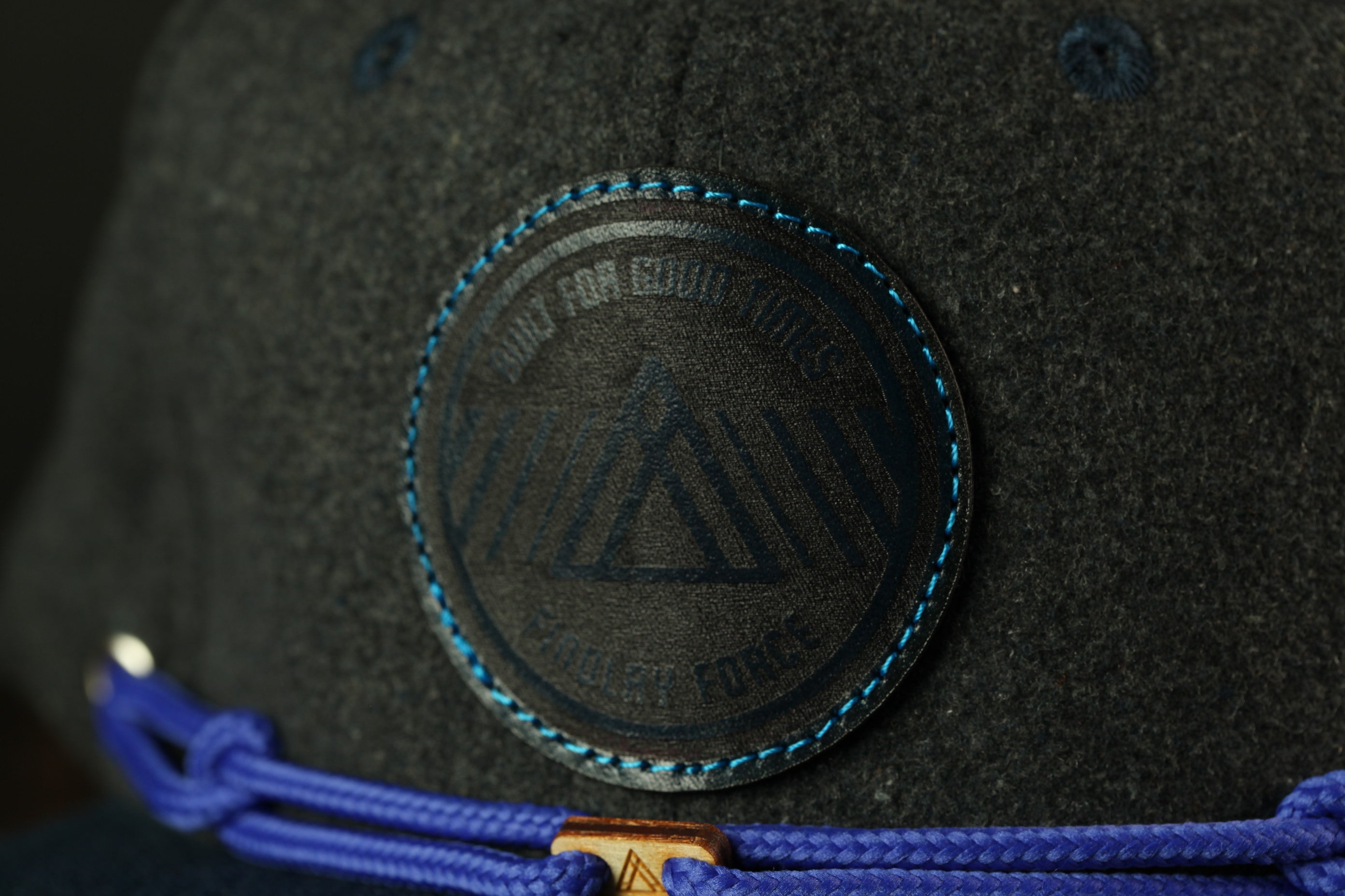 A close-up view of a dark gray fabric with a circular logo featuring a triangle design and the text "MAY FOR EQUITY" printed on it.