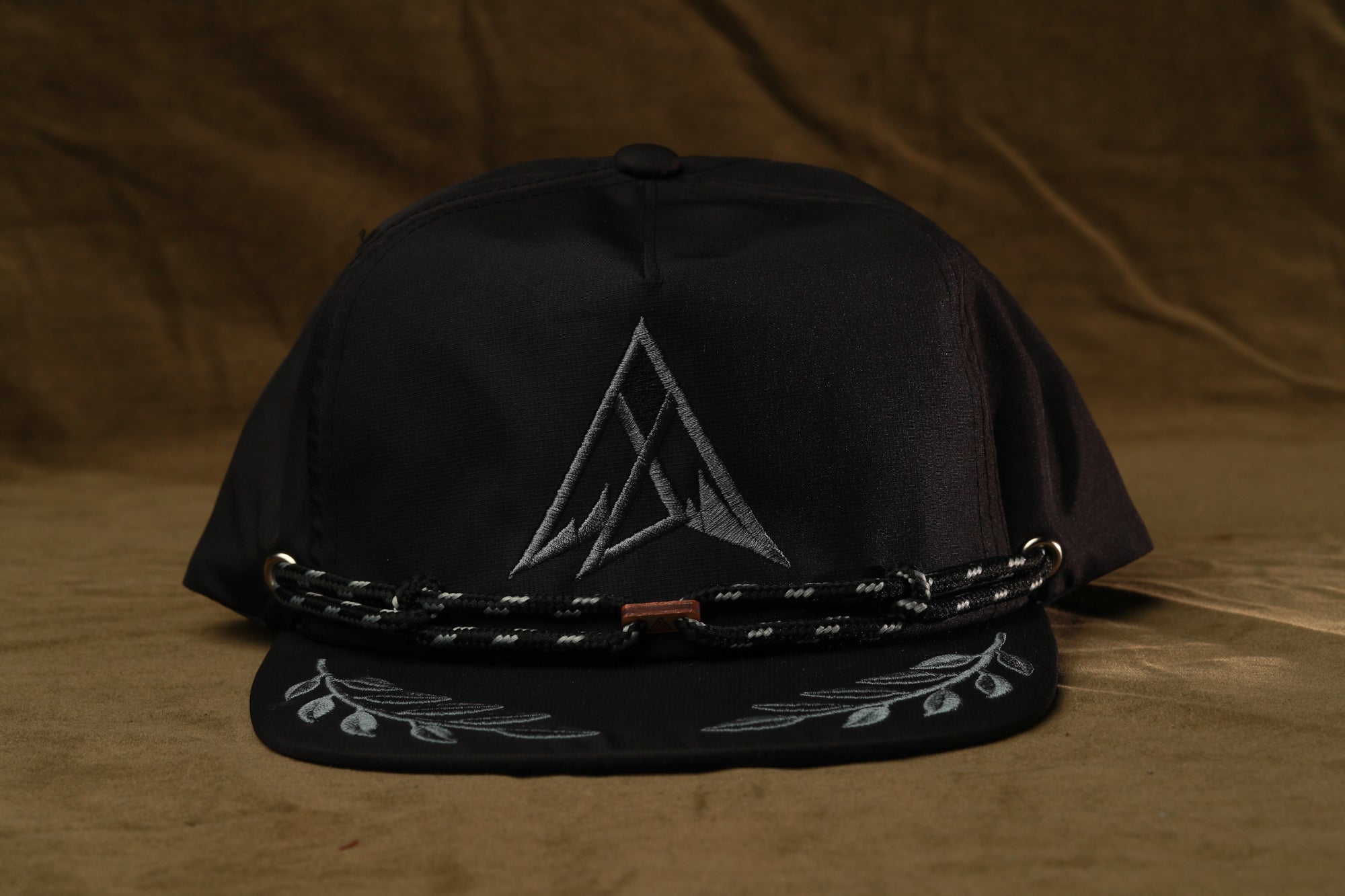 A black baseball cap with a white triangle design on the front and a black braided strap.